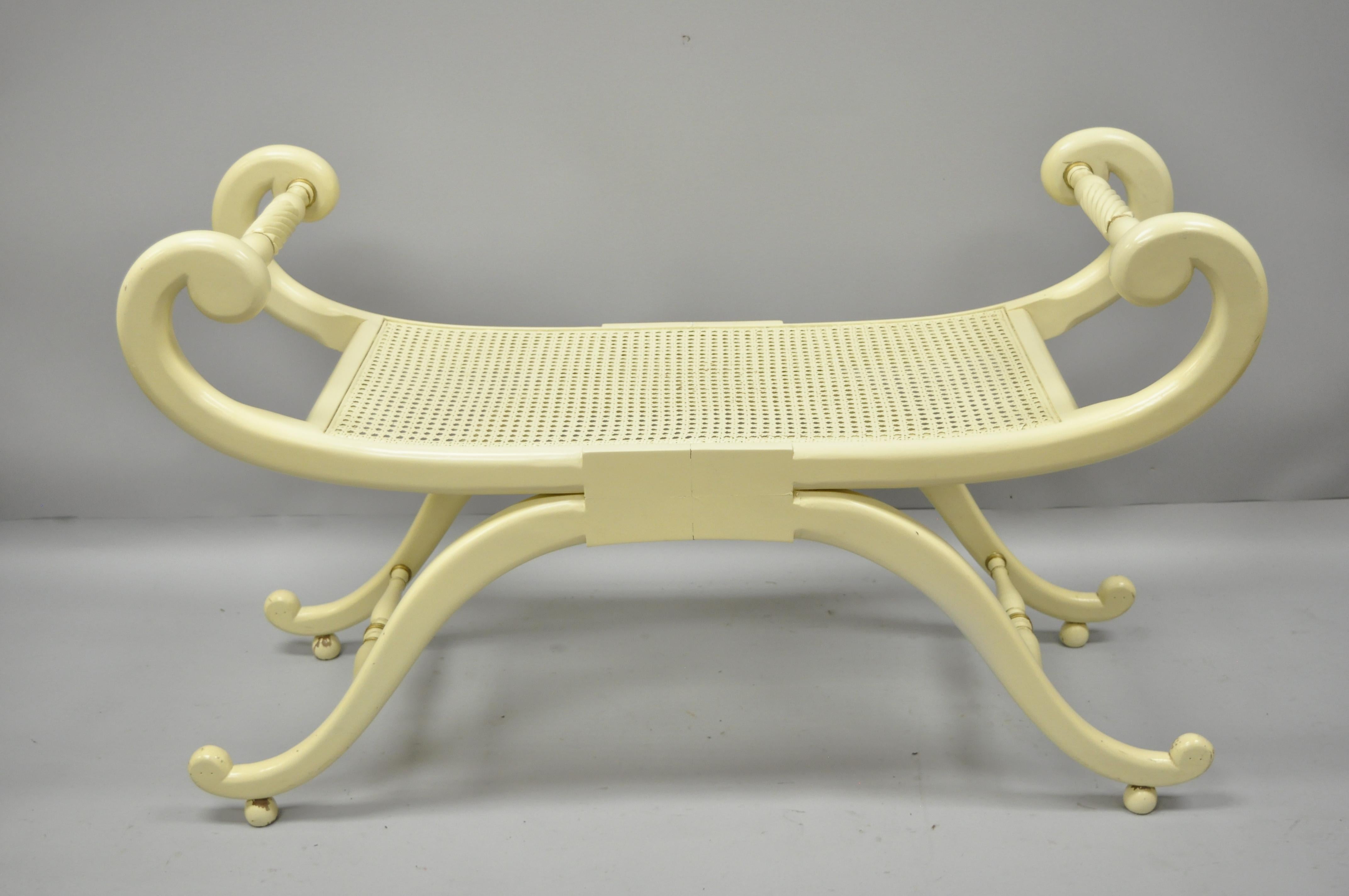 Neoclassical style cane seat Curule X-frame bench. Item features cream and gold painted finish, cane seat, shapely scrolling form, solid wood frame, and great style and form, circa 1960. Measurements: 25