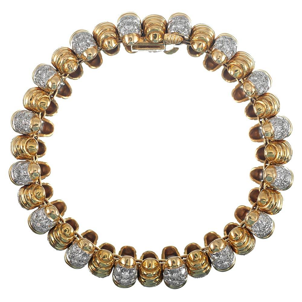 Alternating lengths of textured golden barrels are set with white diamond tips and center stations, encircling the wrist in sculpted sophistication. The piece measures 7.5 inches long and approximately 7/8 of an inch wide. It is set with 9 carats of