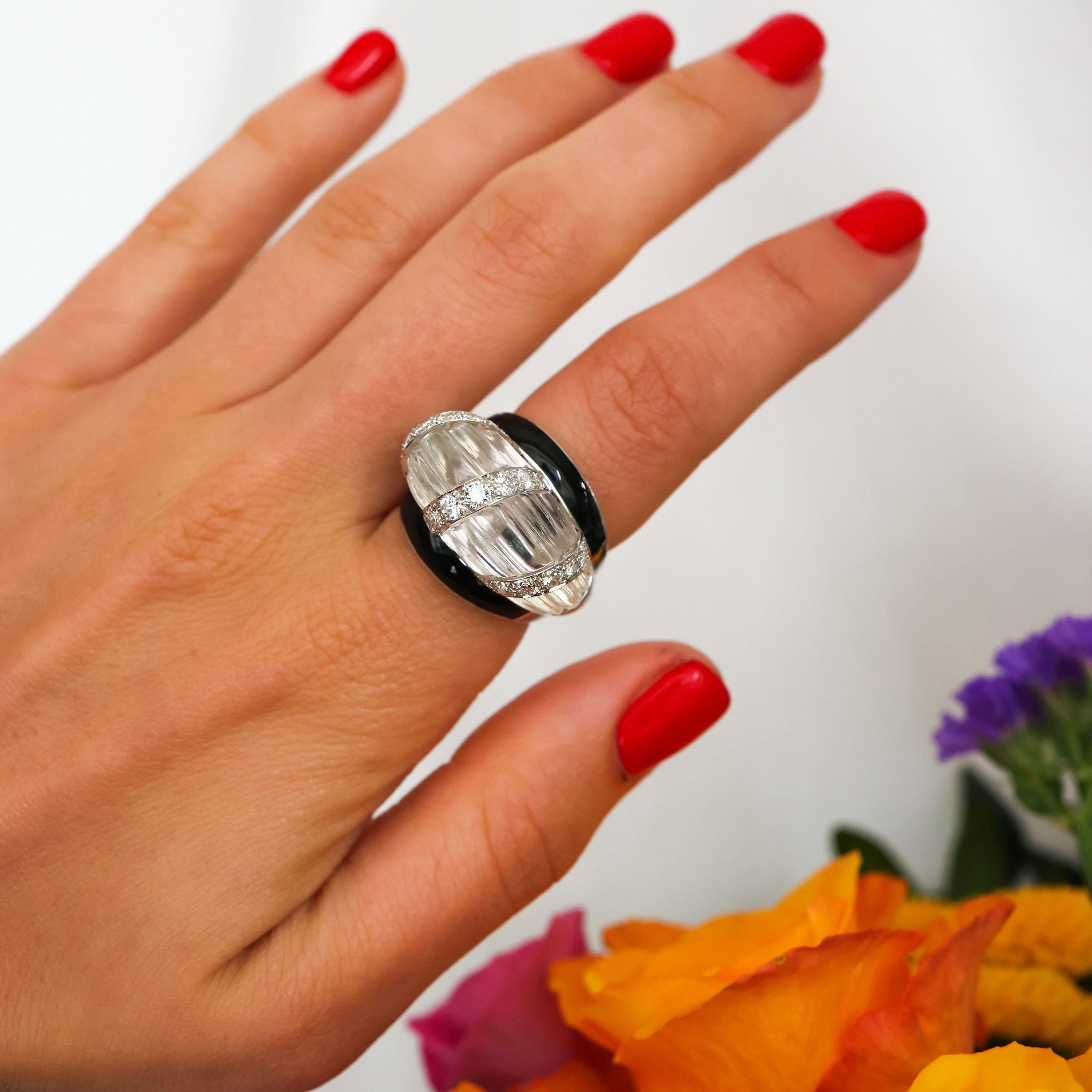 A vintage David Webb bombé style ring, comprised of a raised rock crystal centre, carved to create a horizontal, ribbed design, crossed with three columns of round brilliant-cut diamonds set within it, with black enamel bands either side, mounted in