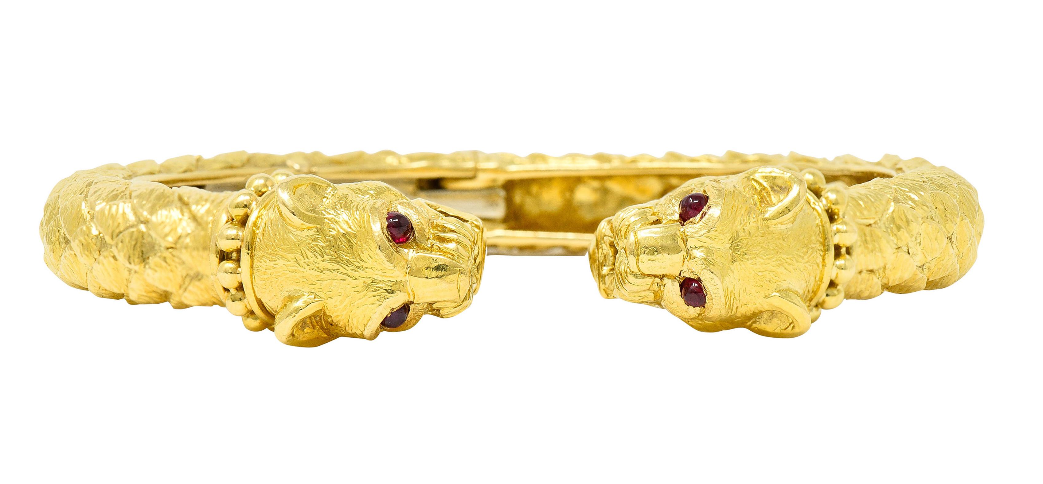 Cuff bracelet designed as two stylized lion heads with texturous scales

Featuring gold bead collars, detailed snarling faces, and textured fur 

Each lion head has two 2.5 mm round ruby cabochon eyes

Rubies are well matched medium in saturation