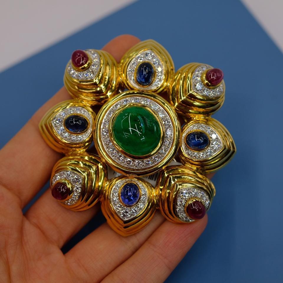 A substantial 18k yellow gold eight-pointed combination brooch/pendant with a large center cabochon emerald, and four each of smaller cabochon blue sapphires and cabochon rubies. Brilliant round diamond pave style borders surround each gem.

By