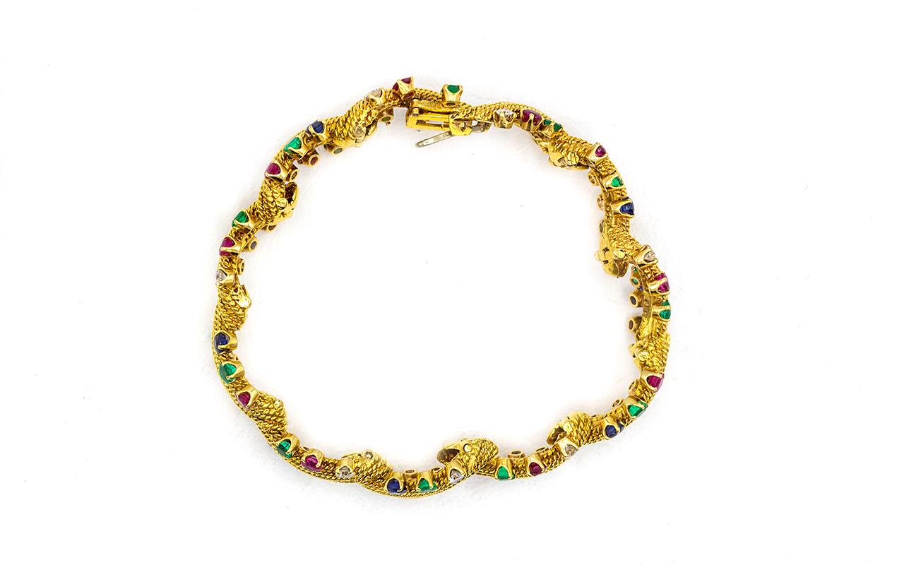 This gem-studded bracelet illustrates the playful side of David Webb, one of the world's oldest and most revered American jewelry houses. The rope textured design is set with rubies, emeralds, sapphires and round-cut diamonds in a classic setting. A