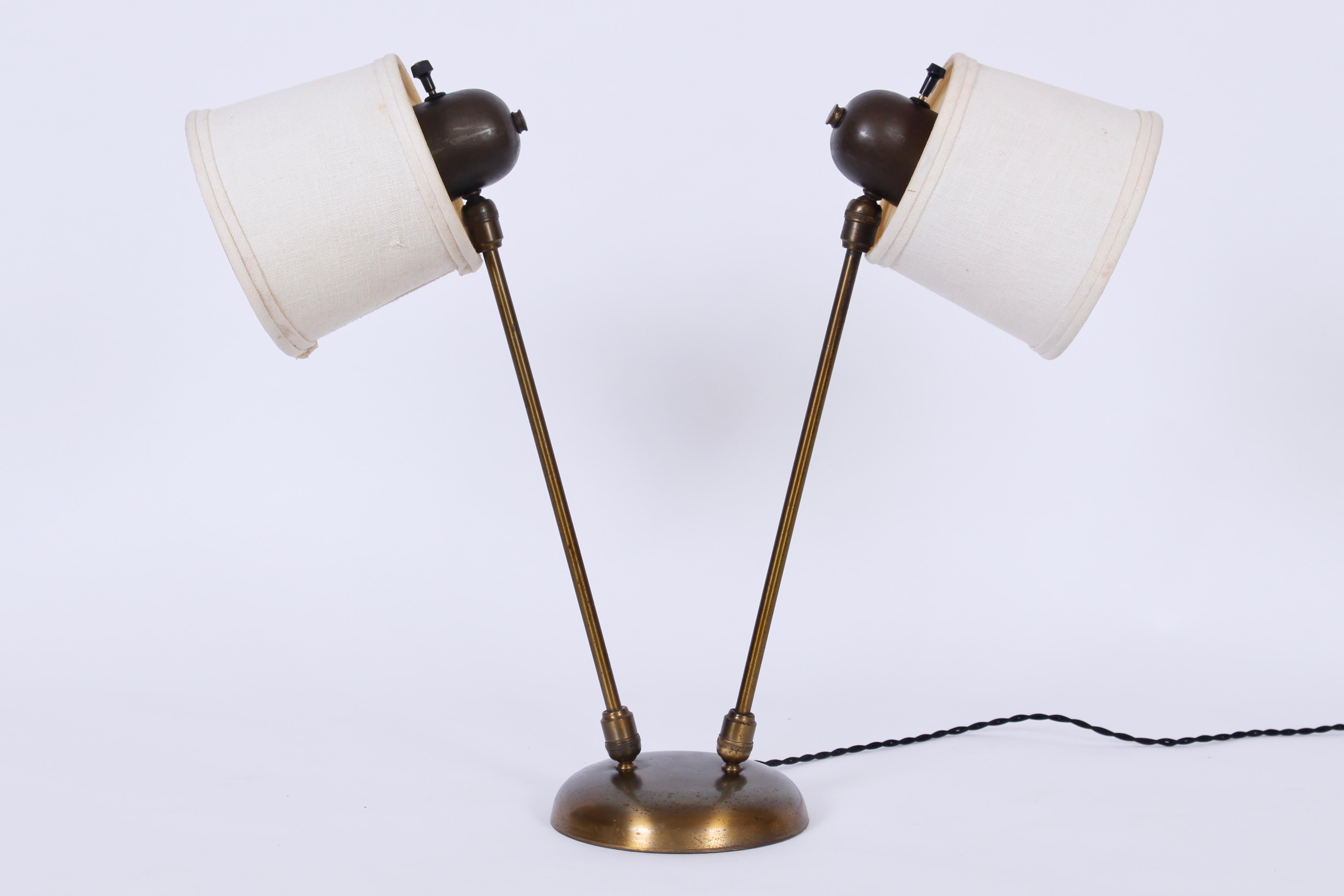 David Wurster articulating two head brass desk lamp.  Featuring finely crafted directional lighting with two adjustable arms, four ball sockets, two natural linen shades, rounded base. Shades (5 H x 5 D top x 6 D bottom).  Early. Modernist. Rarity.