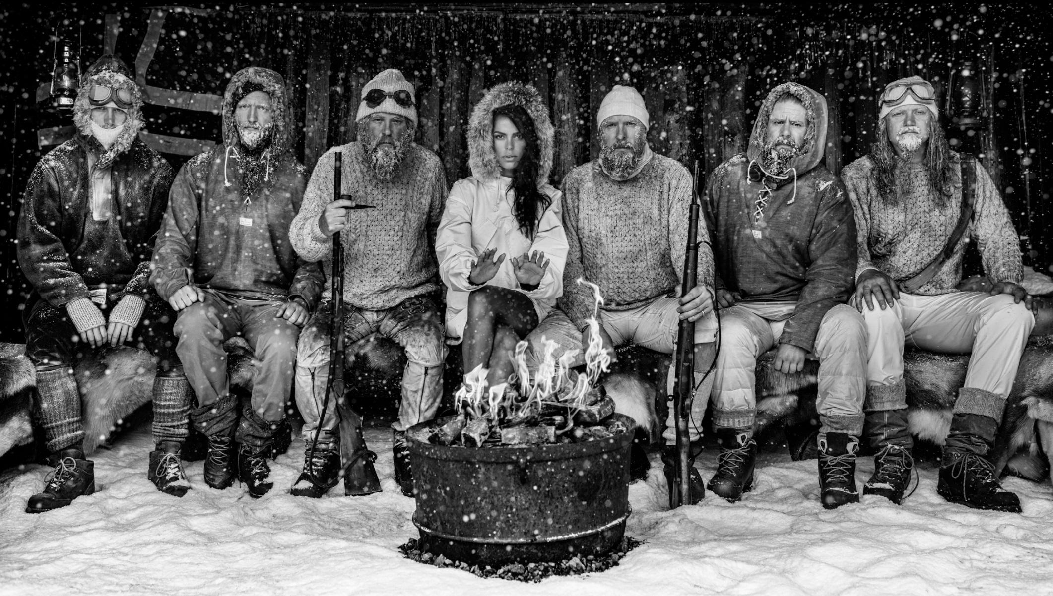 David Yarrow Figurative Photograph - Ice Ice Baby - Model Brooks Nader with Polar Explorers Sitting Around Fireplace