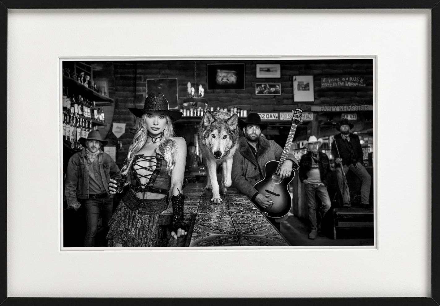 Pappy & Harriet's - Model and Wolf in old Bar, fine art photography, 2024 - Contemporary Photograph by David Yarrow