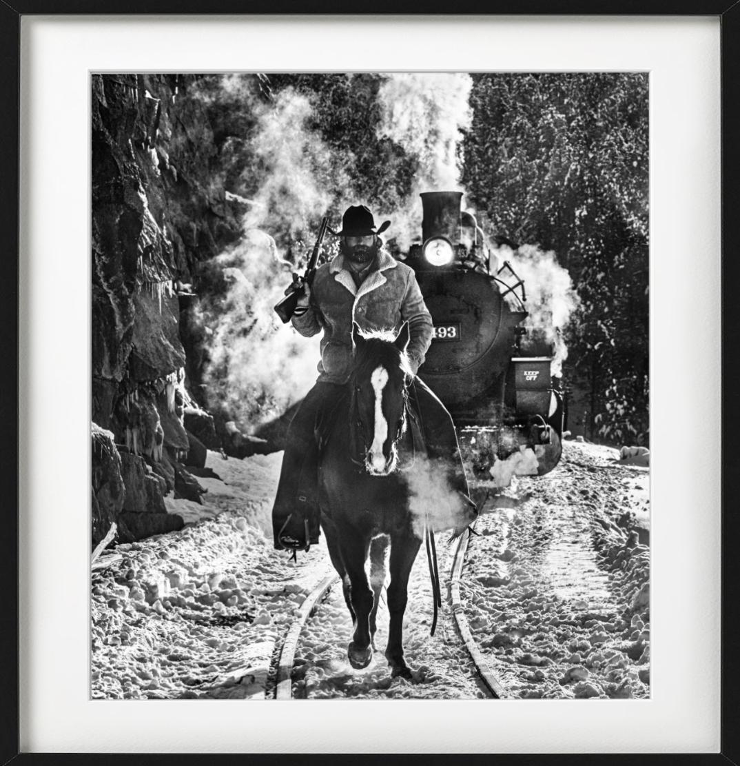 Grim Cowboy Red Dead, cheval chevauchant sur un cheval devant un train à vapeur sauvage - Photograph de David Yarrow