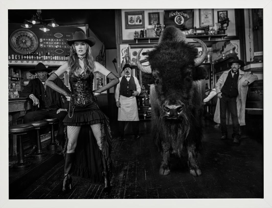 Roulette russe - Modèle et bison dans un bar occidental, photographie d'art, 2024 - Photograph de David Yarrow
