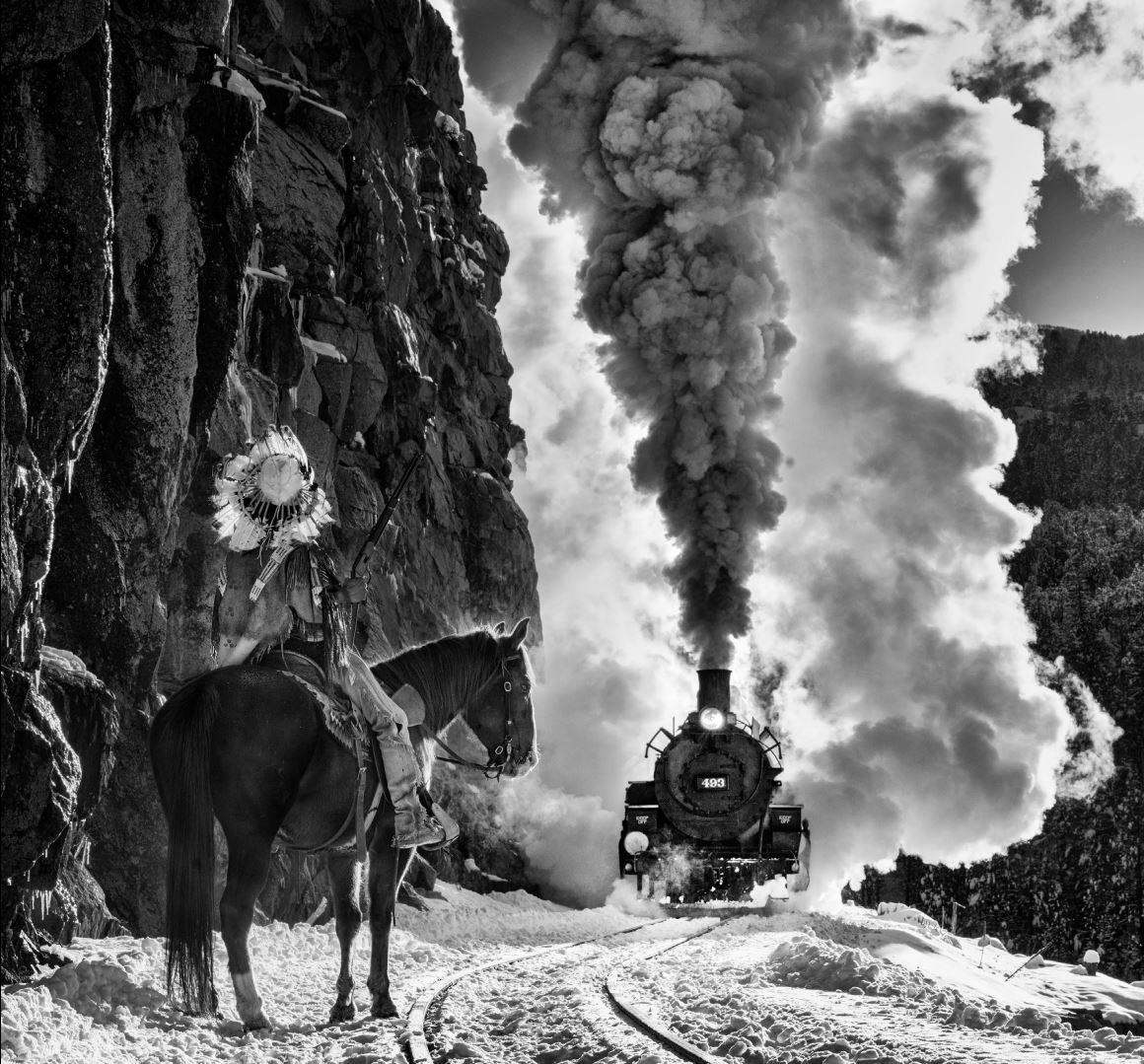 The Manifest Destiny - b&w photograph showing a train and a native american 