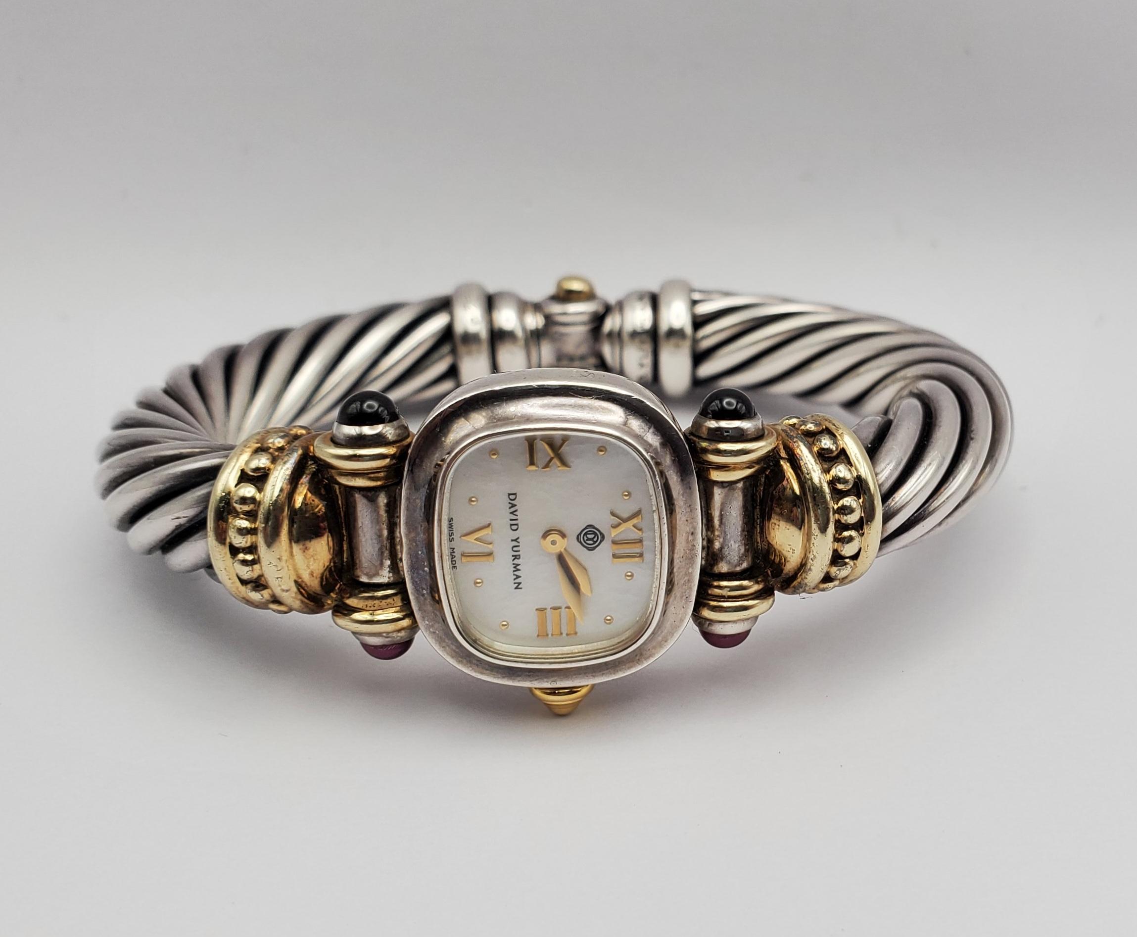 David Yurman 10mm Cable Collection bangle watch. The watch features four bezel set cabochon garnet stones and a mother of pearl dial. The piece is crafted in sterling silver and 14k gold with a sapphire crystal. The stylish bangle bracelet adds a