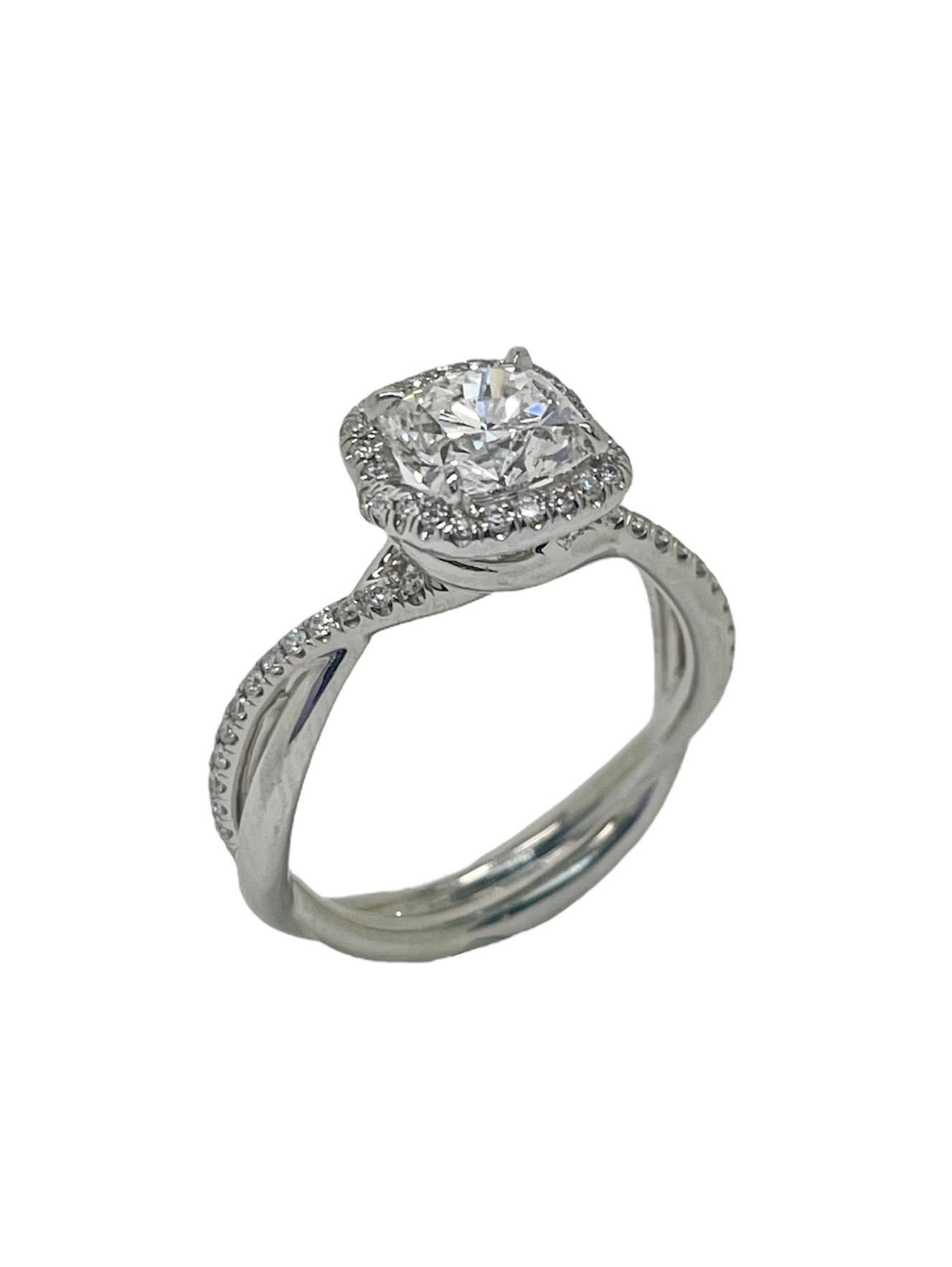 This elegant engagement ring contains a 1.22 carat cushion brilliant cut diamond, E color and SI1 clarity, this diamond is a stunner! The band, in a twisted infinity design symbolizing two lives coming together, with pave round brilliant cut