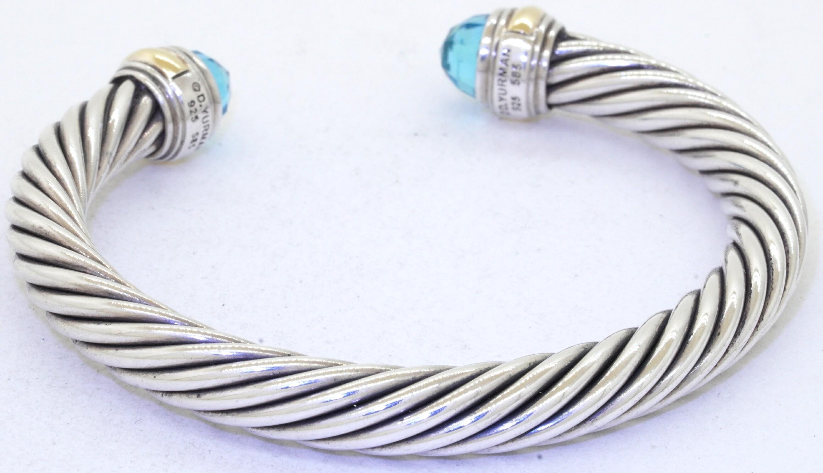 David Yurman 14K gold & 925 Sterling silver Blue topaz cuff bracelet. This outstanding piece of jewelry is crafted in both 14K gold/Sterling silver and features 2 genuine approx. 7mm diameter Blue topaz gems. These Fancy cut gems are bezel set, on