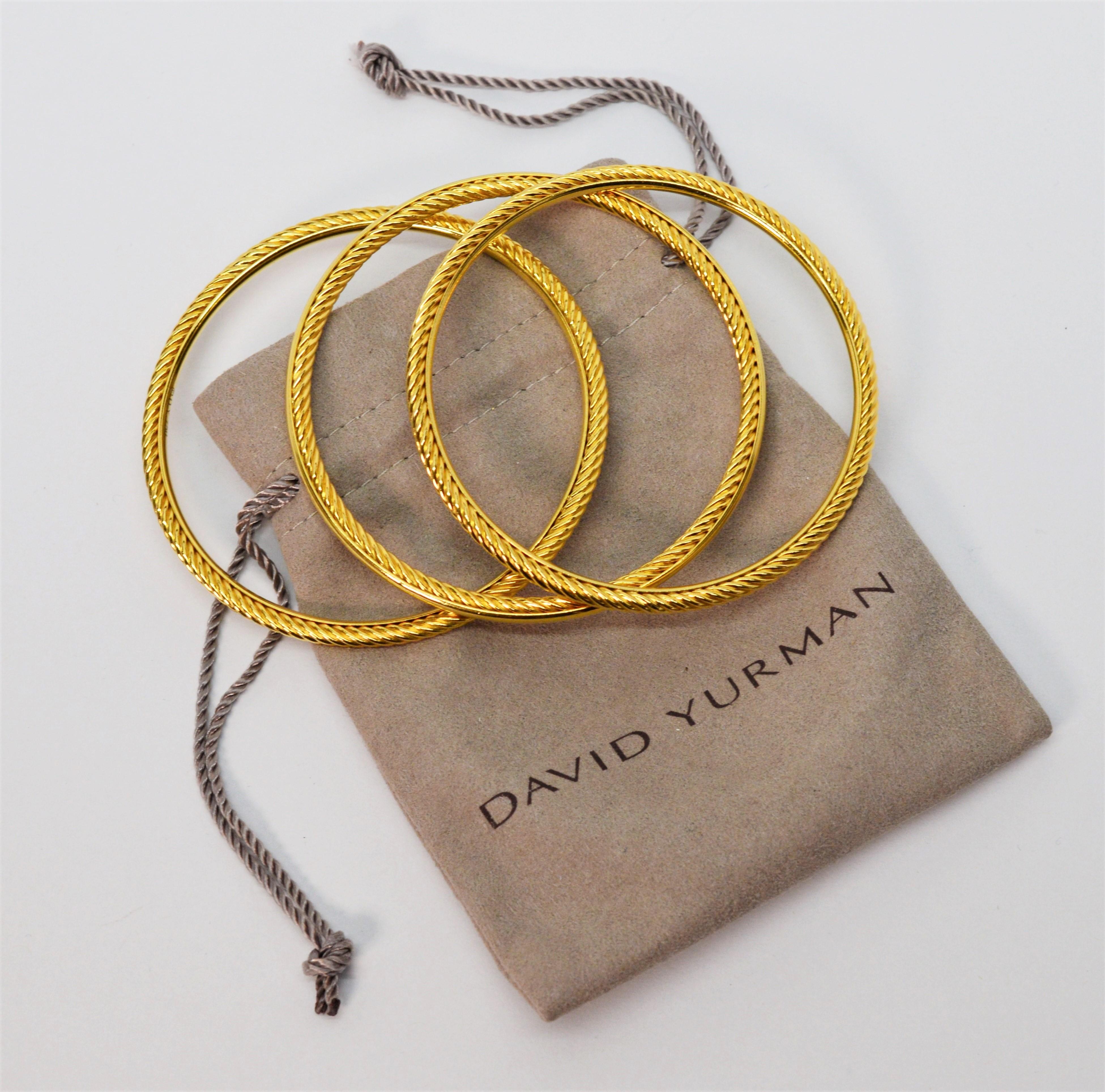 Always fashionable and stackable, a set of three eighteen karat 18k yellow gold bangle bracelets by David Yurman. Appointed with classic DY elements, the trio includes two with an outside cable detail and the third bracelet has a complementing