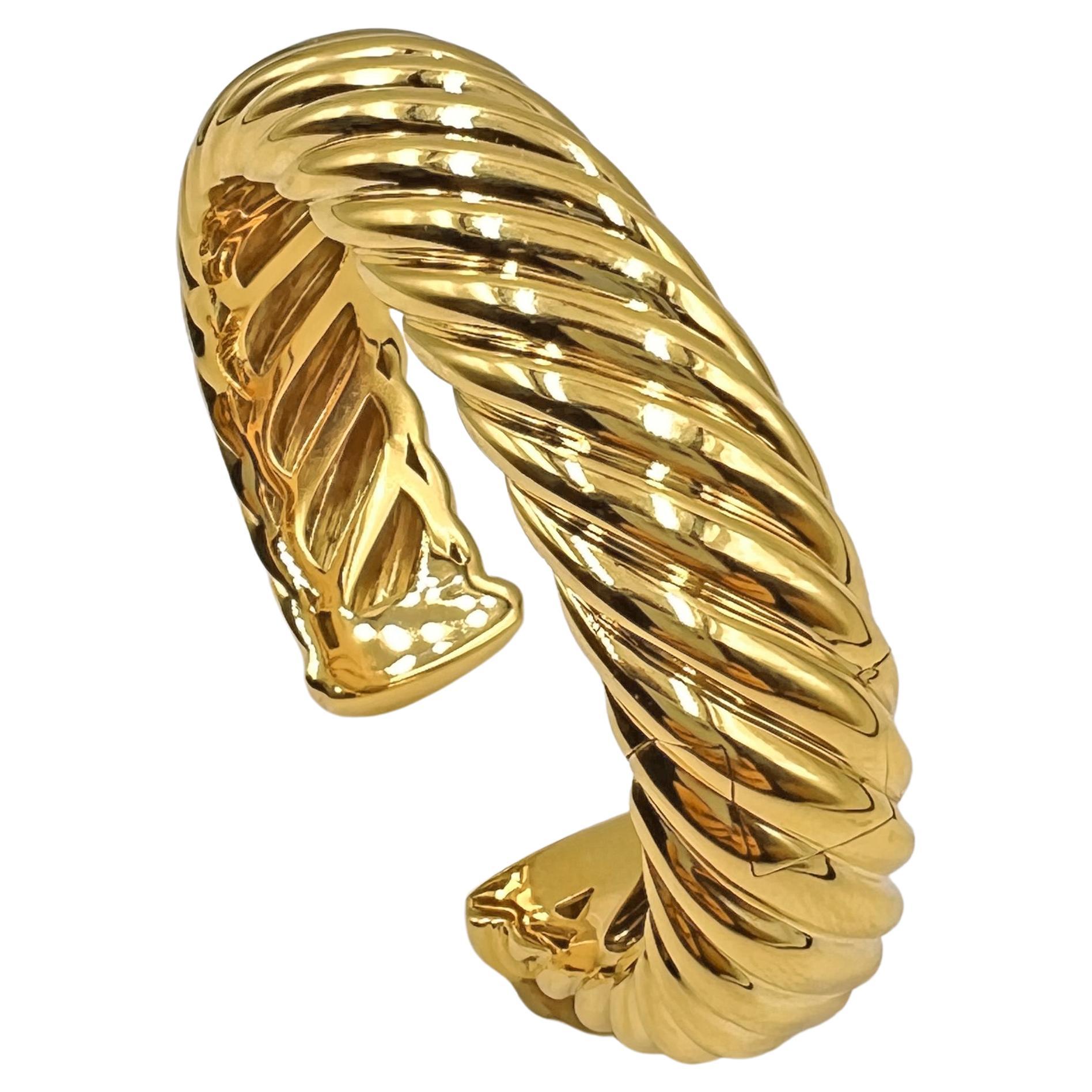 David Yurman oval-shaped cuff bracelet in polished 18k yellow gold.  Diagonal groove design with an open back and hinge on one side to allow for easy fitting on the wearer's wrist.  Measuring 15.5mm in width.  Signed 