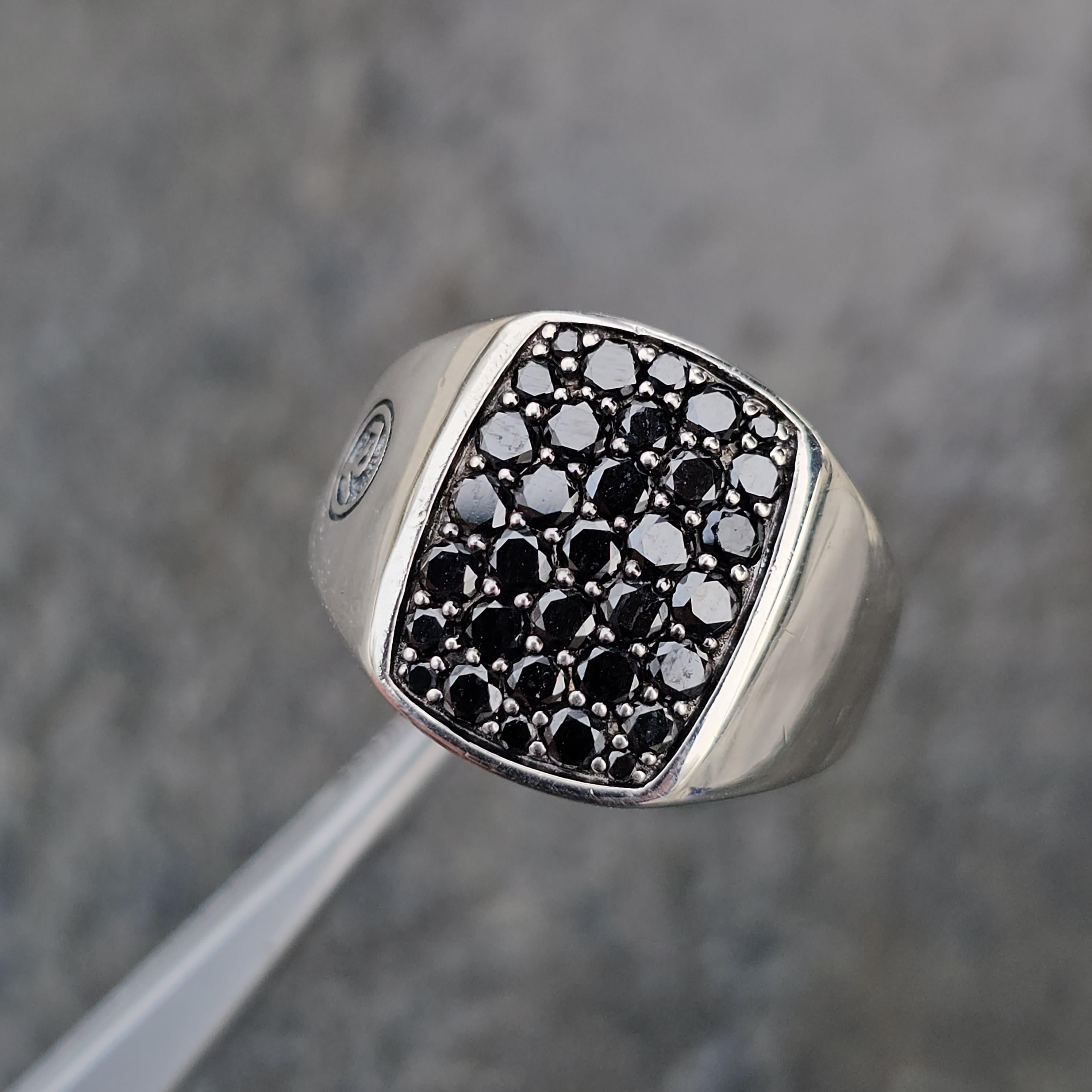 Presenting a striking David Yurman signet ring crafted in sterling silver, adorned with a captivating array of black diamonds. The ring showcases a bold, rectangular face encrusted with meticulously set black diamonds, creating a mesmerizing, dark