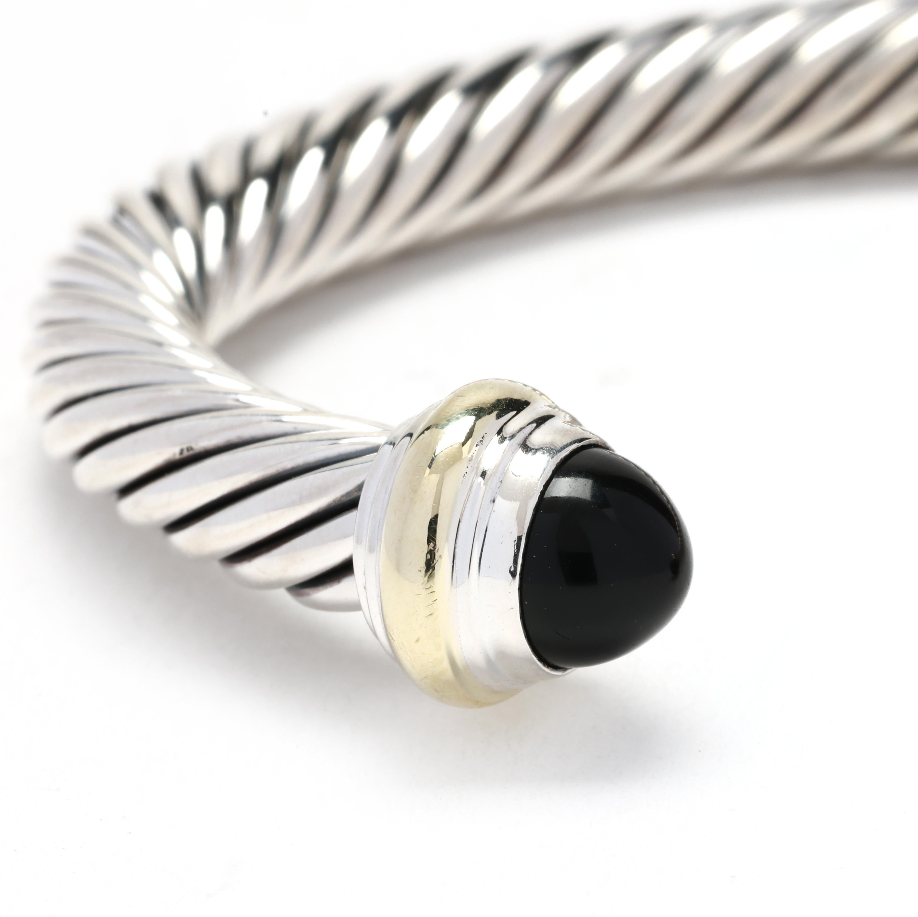This classic David Yurman black onyx cable classic cuff bracelet is an iconic piece from the celebrated designer. Crafted from sterling silver and accented with 14k yellow gold, this bracelet features a black onyx gemstone at the center, adding a