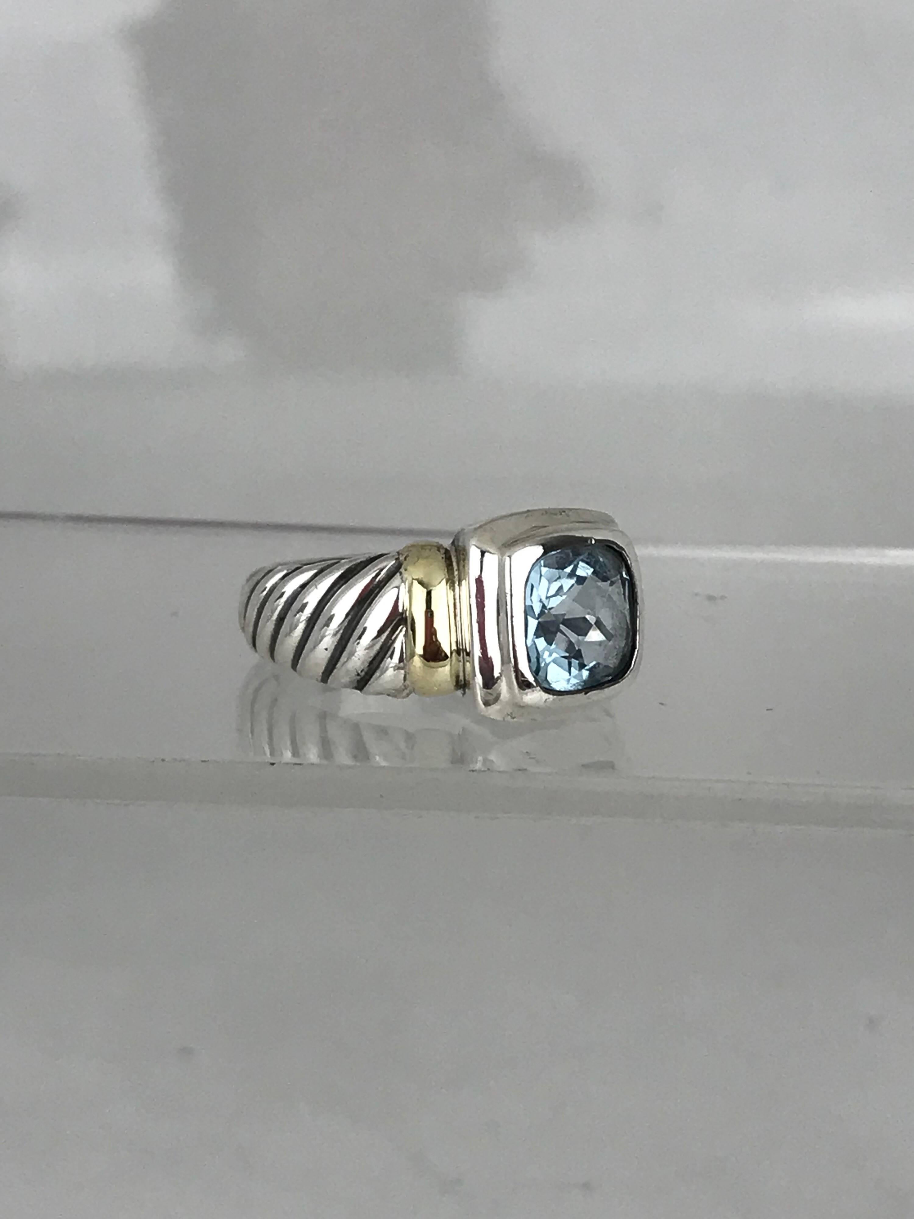 David Yurman ring with a center blue topaz, cushion cut gemstone measuring 8.55 millimeters in diameter. 
The metal is sterling silver with an accenting, yellow gold 14 karat section on either side of the center stone.
The ring size is size 7
Circa