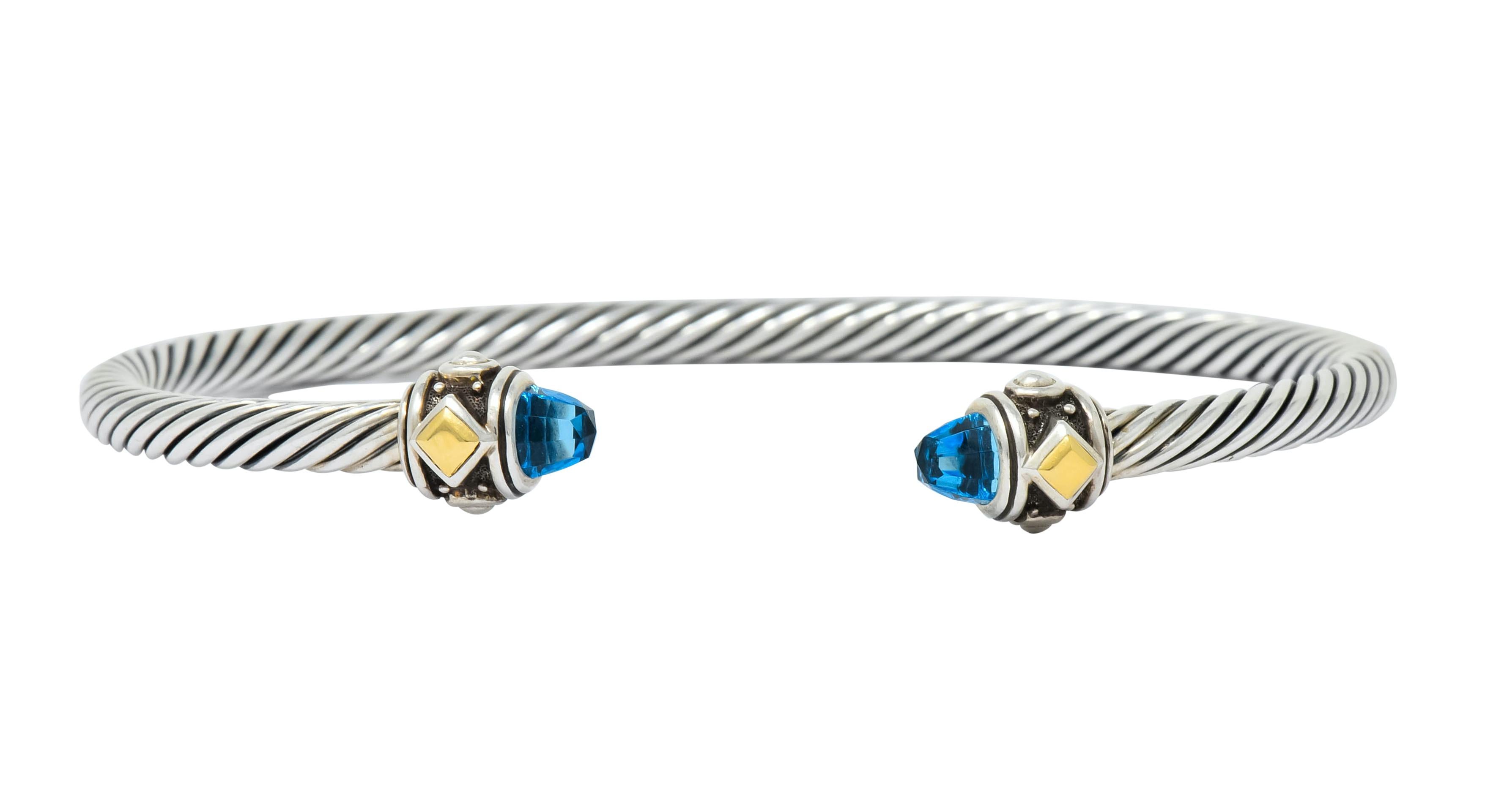 Cuff style bracelet comprised of sterling silver twisted cable motif

Terminating as two faceted blue topaz bullet cabochon, transparent and brilliantly sky blue in color

Bezel set in silver terminals featuring a recessed channel accented by gold