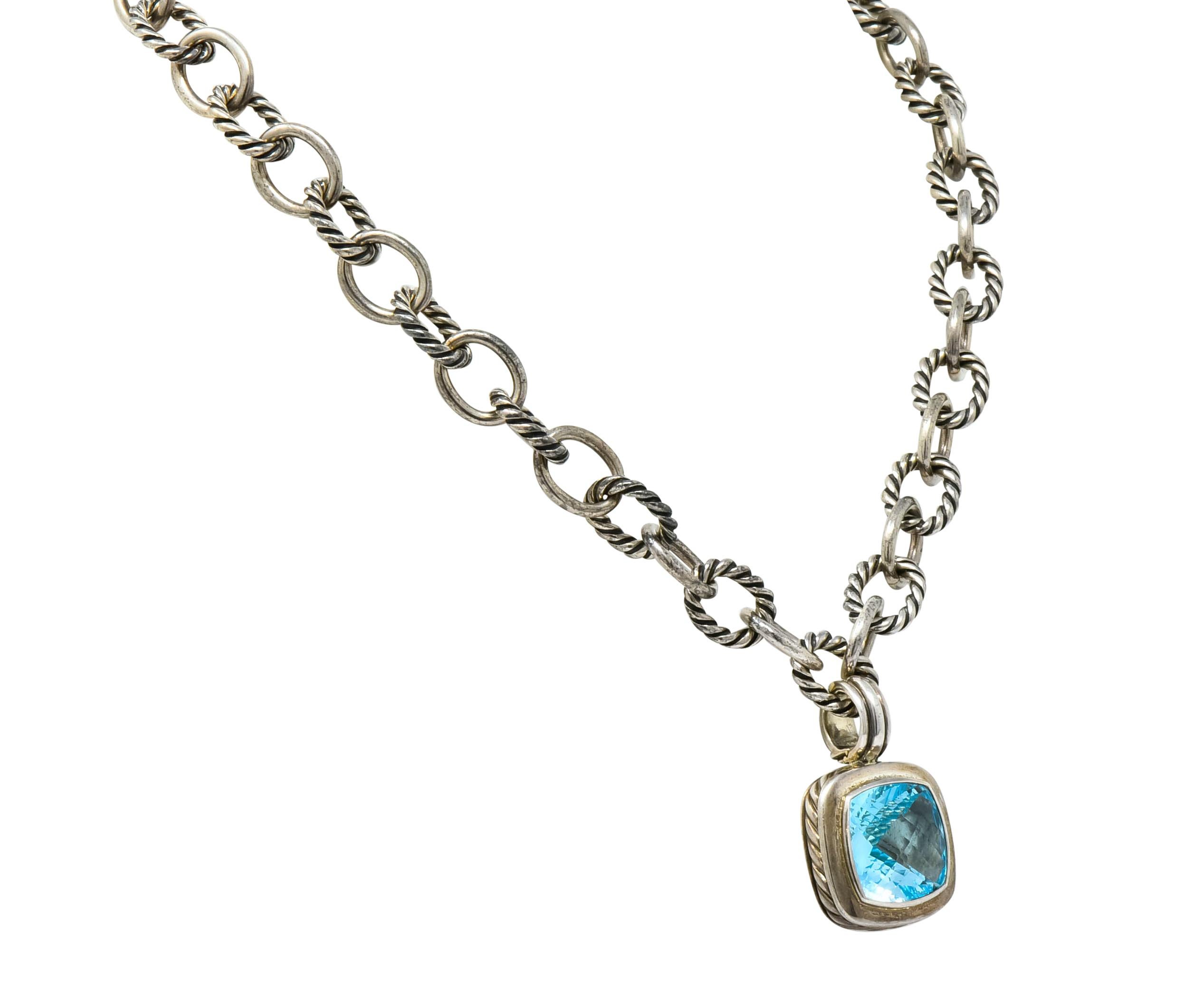 Centering a faceted cushion cut blue topaz, transparent and a saturated electric blue color

Bezel set in a polished silver surround with a ribbed, hinged bale and accented by twisted cable motif

Accompanied by necklace comprised of smooth oval