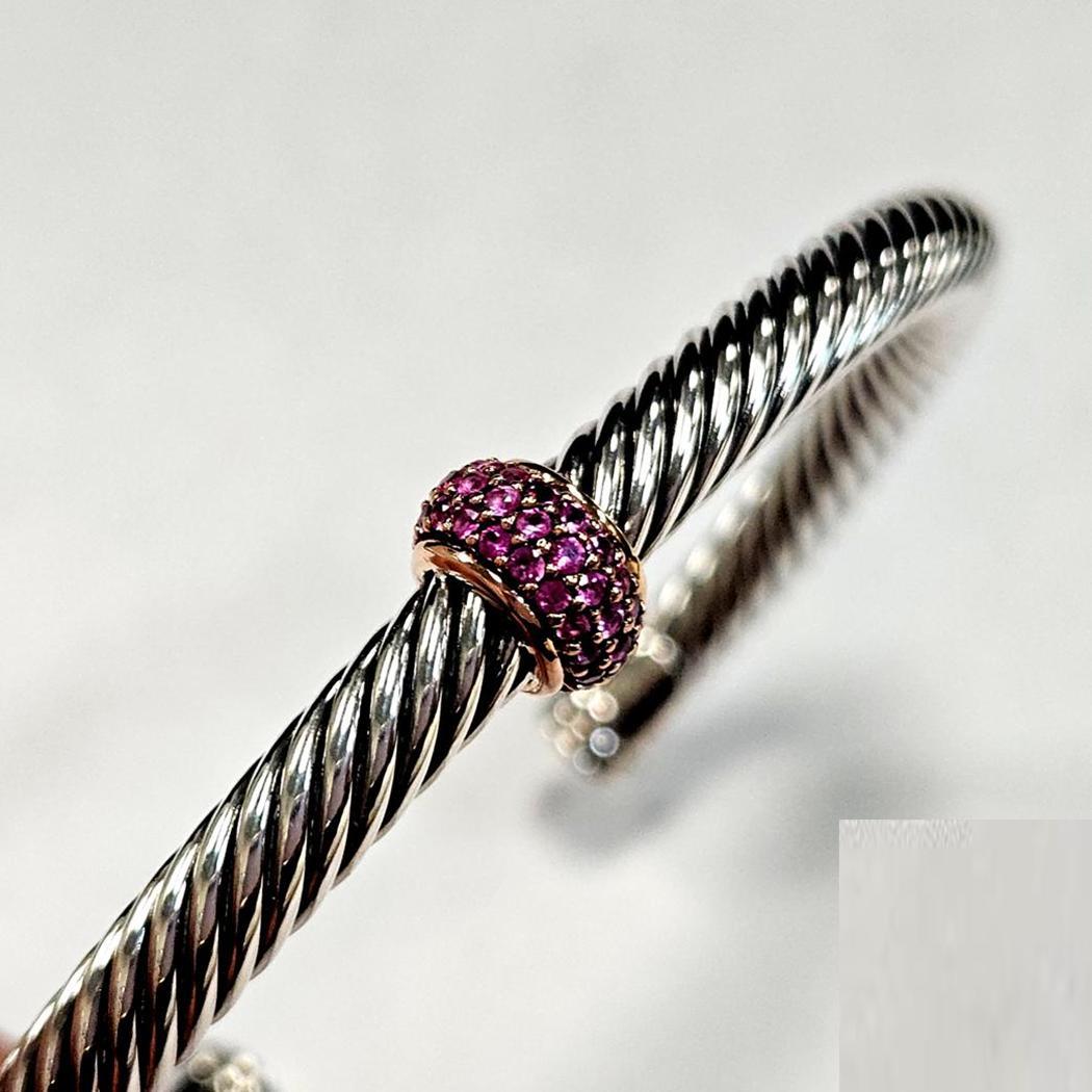 Questo bracciale David Yurman Cable Candy esemplifica la fusione di forme audaci e materiali pregiati tipica del designer. Realizzato in argento sterling con accenti in oro rosa 18 carati, il pezzo è evidenziato da una sezione di zaffiri rosa