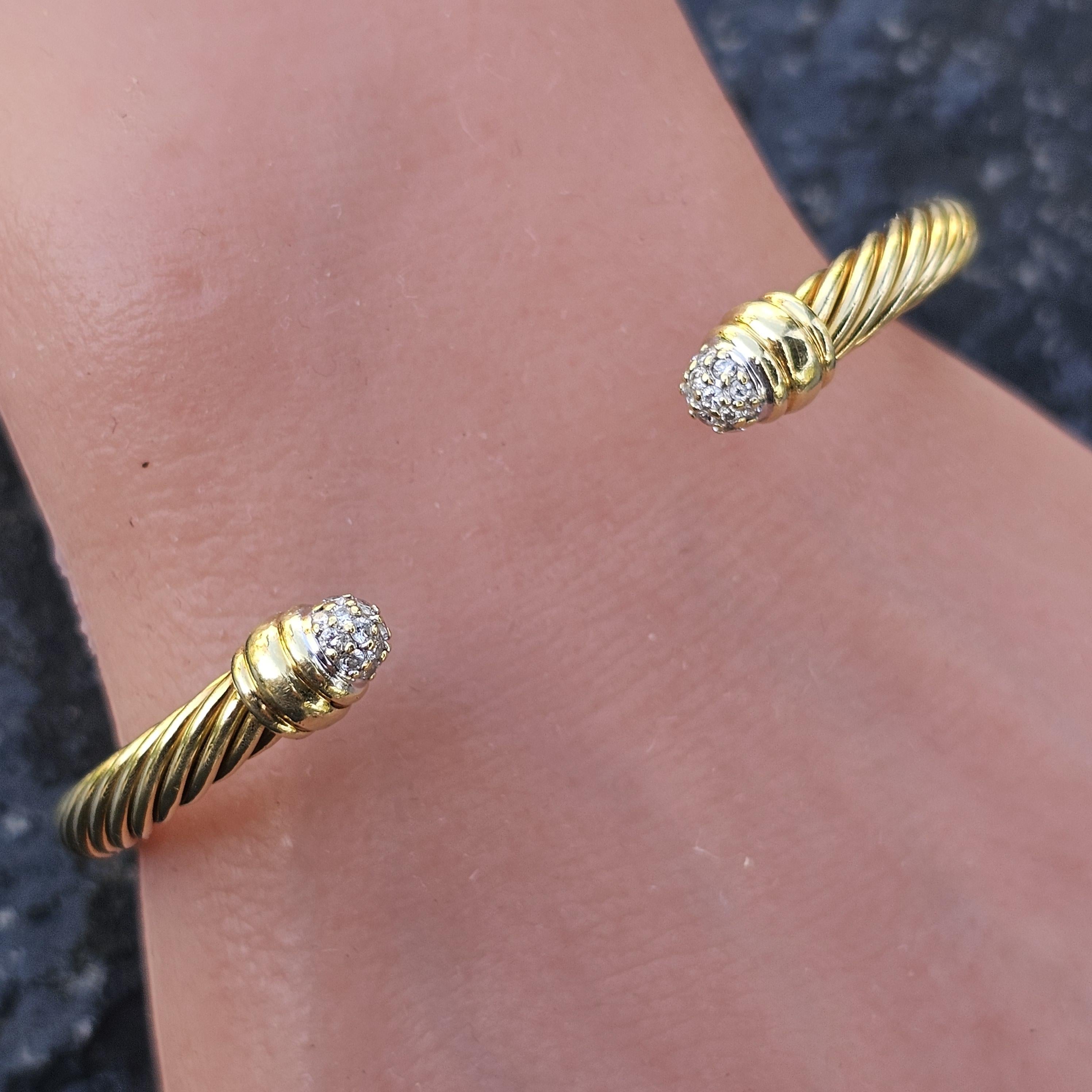 Este brazalete David Yurman es un impresionante ejemplo de lujo y diseño modernos. Elaborado en oro amarillo de 18 quilates, presenta un motivo de cable trenzado que destila sofisticación. La pulsera está adornada con diamantes blancos en cada