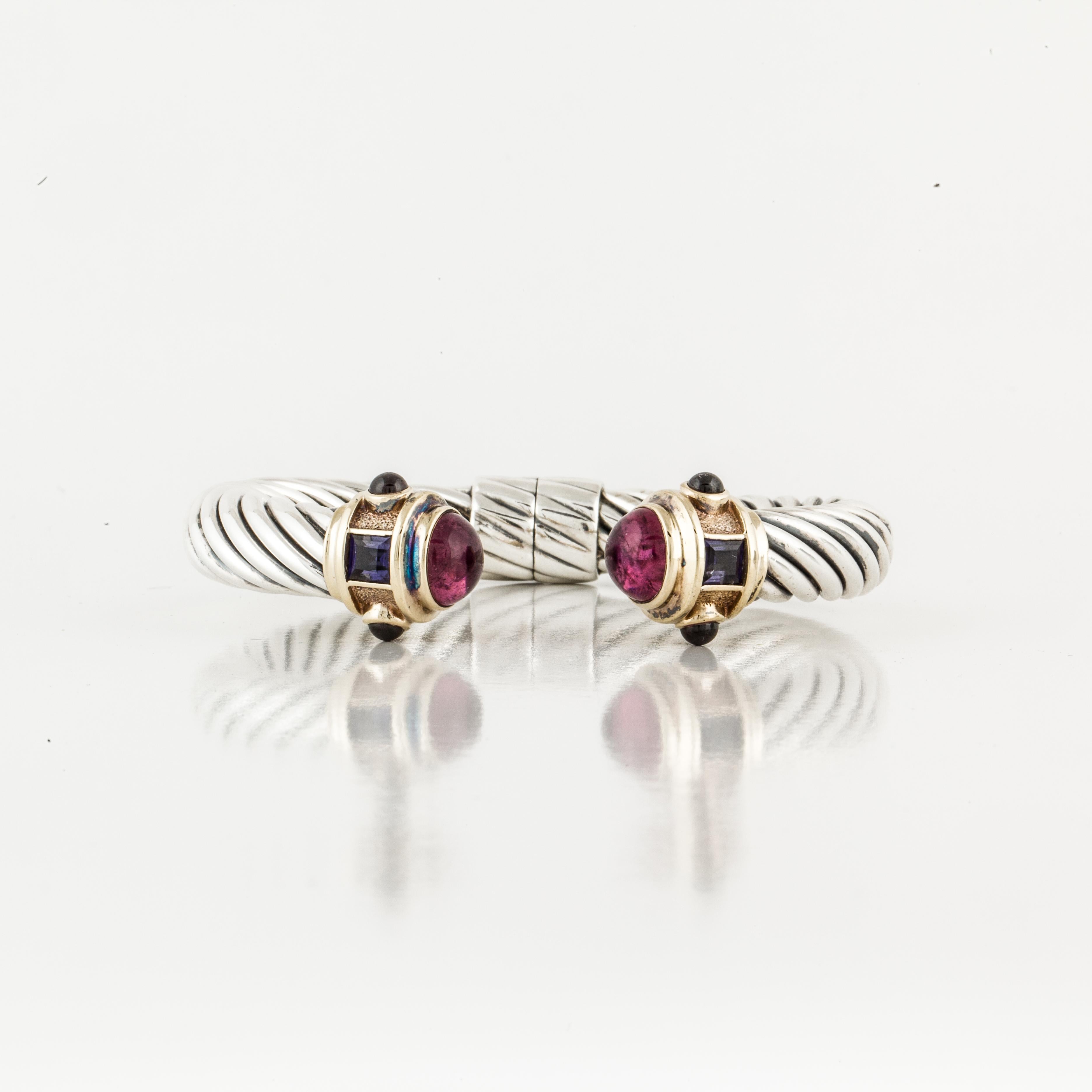 Sterling silver and 14K yellow gold classic cable cuff bracelet by David Yurman.  Features two (2) square faceted iolites, four round cabochon amethysts and two round cabochon pink tourmalines.  Hinged at the bottom.  Measures 2 1/8 inches at the