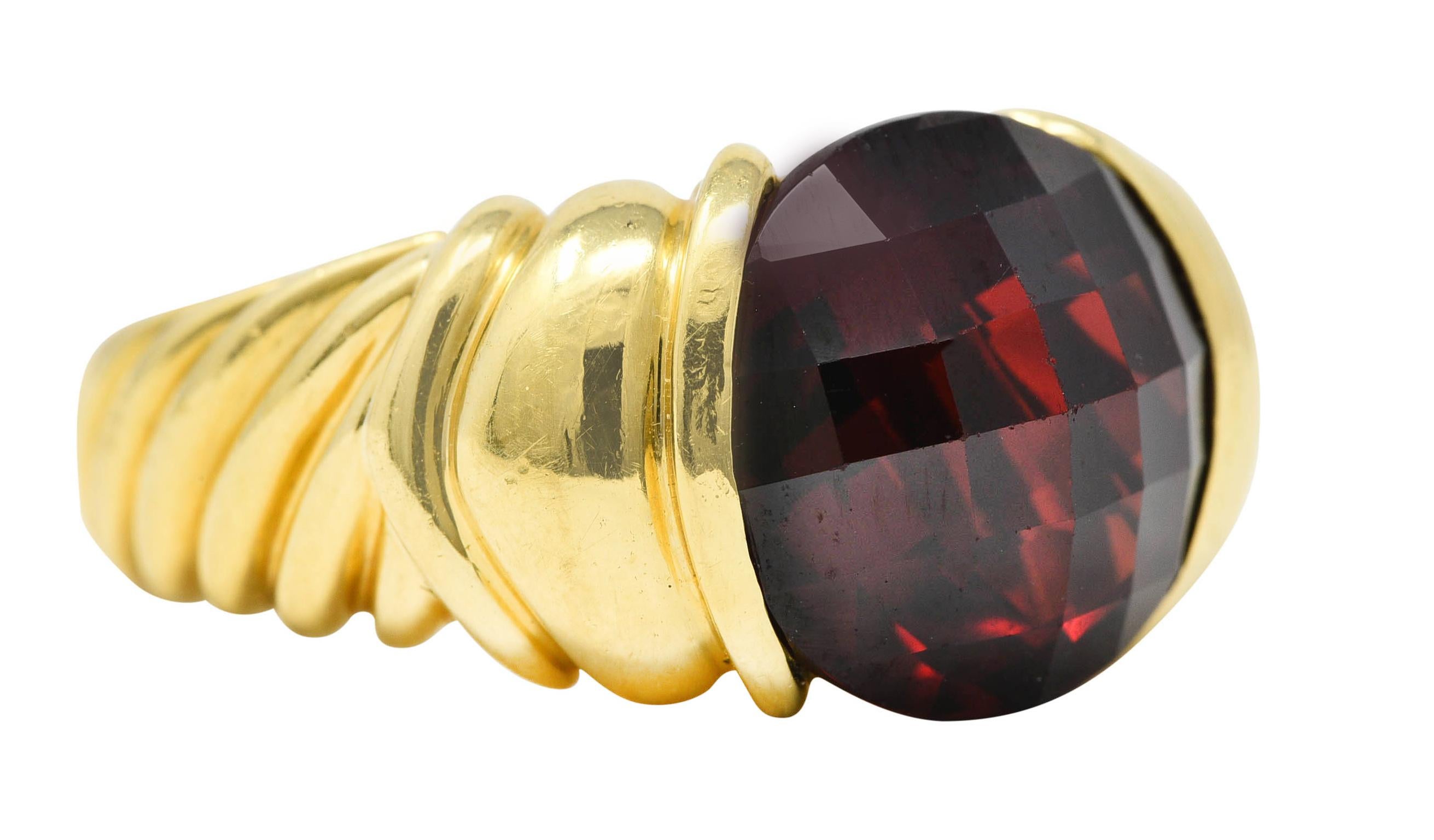 Centering a 12.0 mm round checkerboard cut garnet - transparent deep red. Set in partial bezel and flanked by ridged shoulders. With twisted cable motif shank. Stamped 750 for 18 karat gold. With maker's mark for David Yurman. Circa: 2000's from the