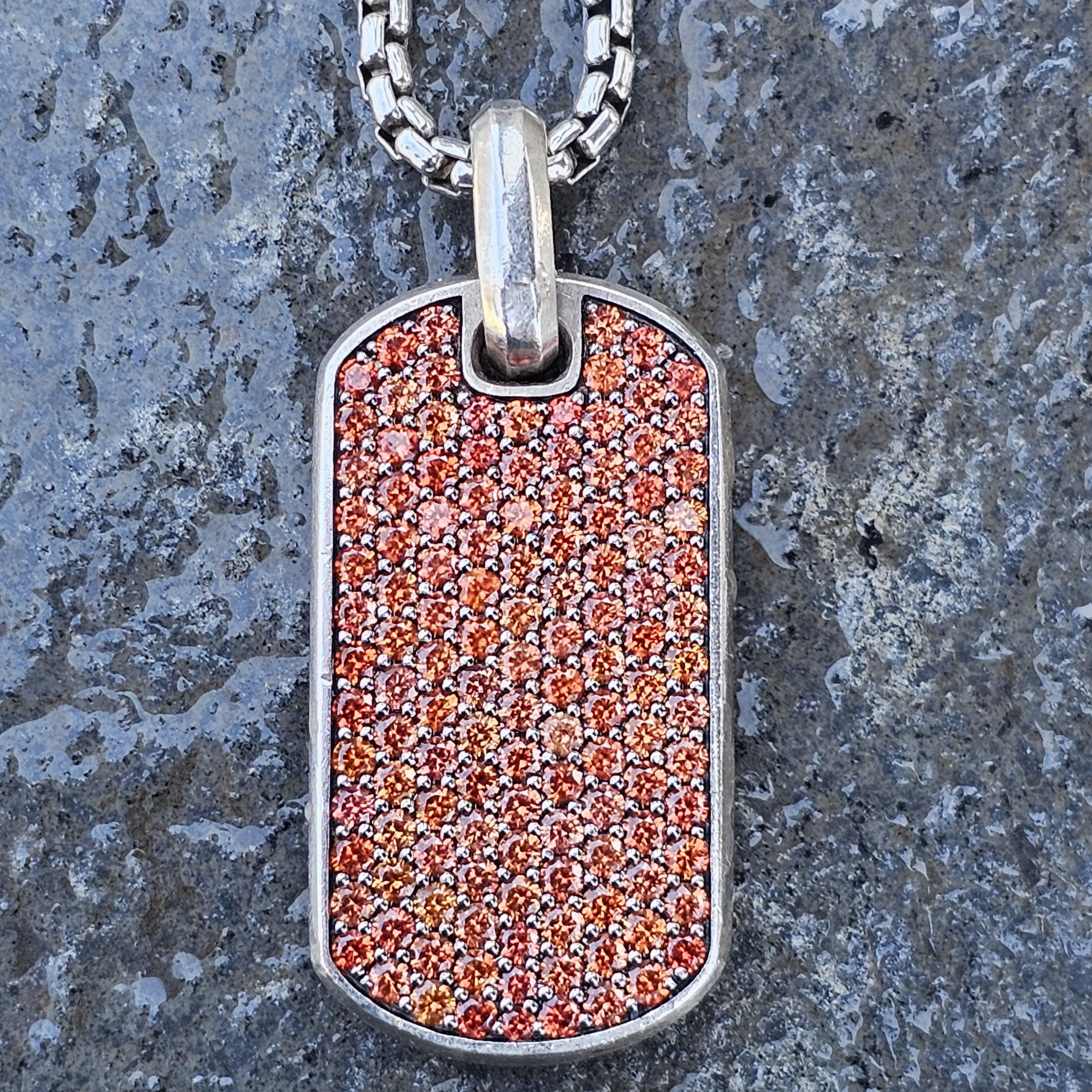 This David Yurman Chevron 35mm orange sapphire pendant necklace is a striking piece of jewelry that adds a touch of elegance to any ensemble. The necklace features a robust sterling silver chain, measuring 26 inches in length, providing a