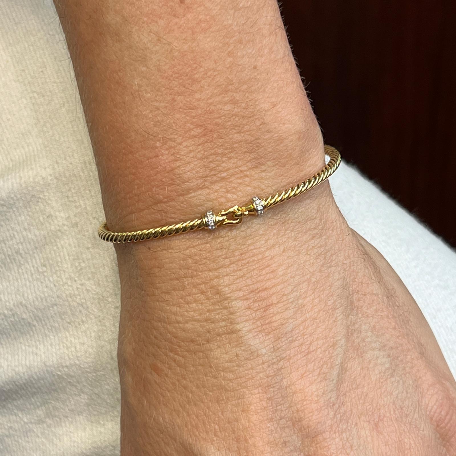 Diamond buckle cable bracelet by designer David Yurman fashioned in 18 karat yellow gold. The cable bangle features round brilliant diamonds weighing approximately .05 CTW on the hook clasp. The bracelet measures 2.6mm in width, 2.25 inches in