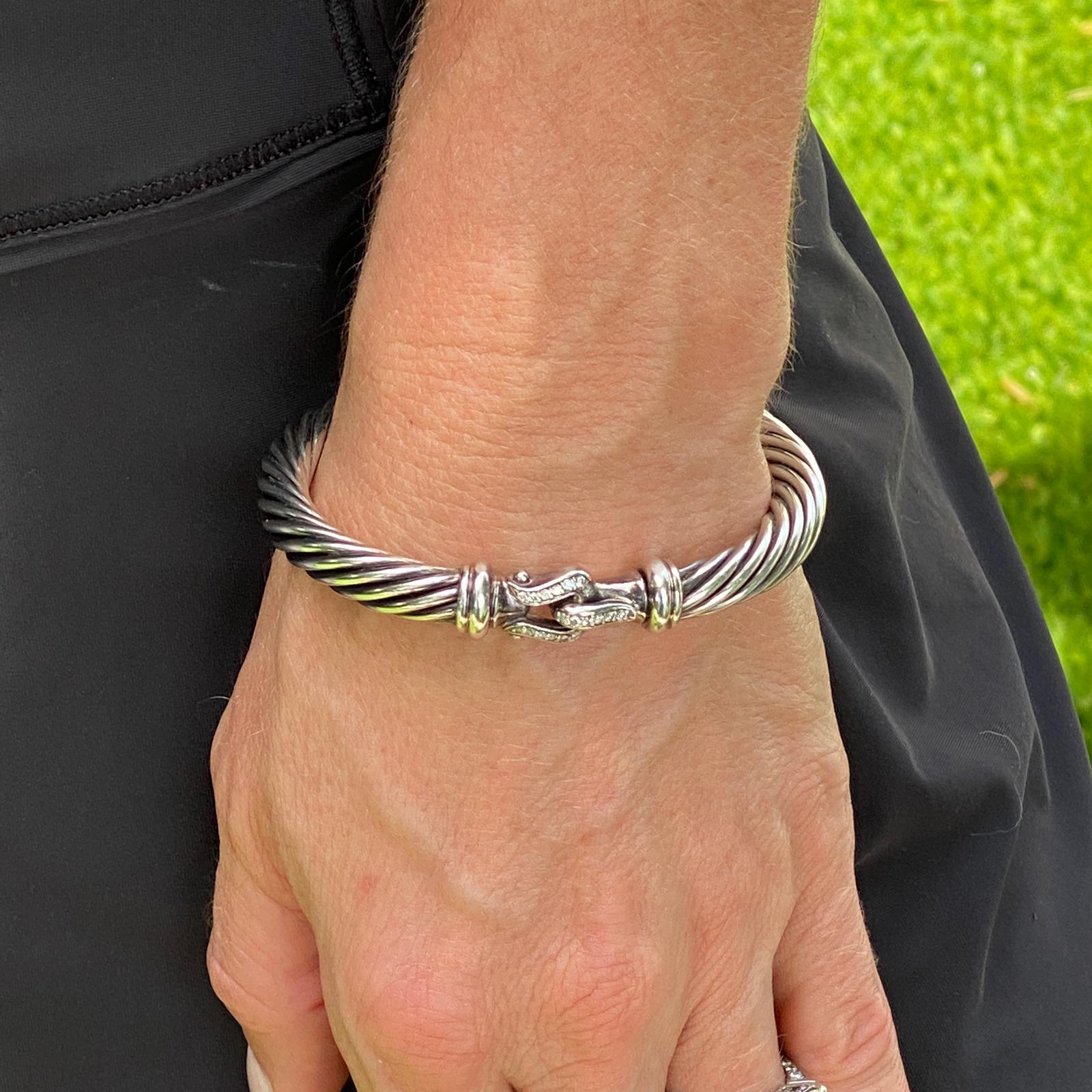 David Yurman Diamond Buckle Cable Cuff aus Sterlingsilber. Auf der Schnalle befinden sich runde Diamanten im Brillantschliff mit einem Gesamtgewicht von etwa 0,18 Karat. Die 7mm Manschette misst 2,25 Zoll im Durchmesser (mittlere Größe) und ist mit