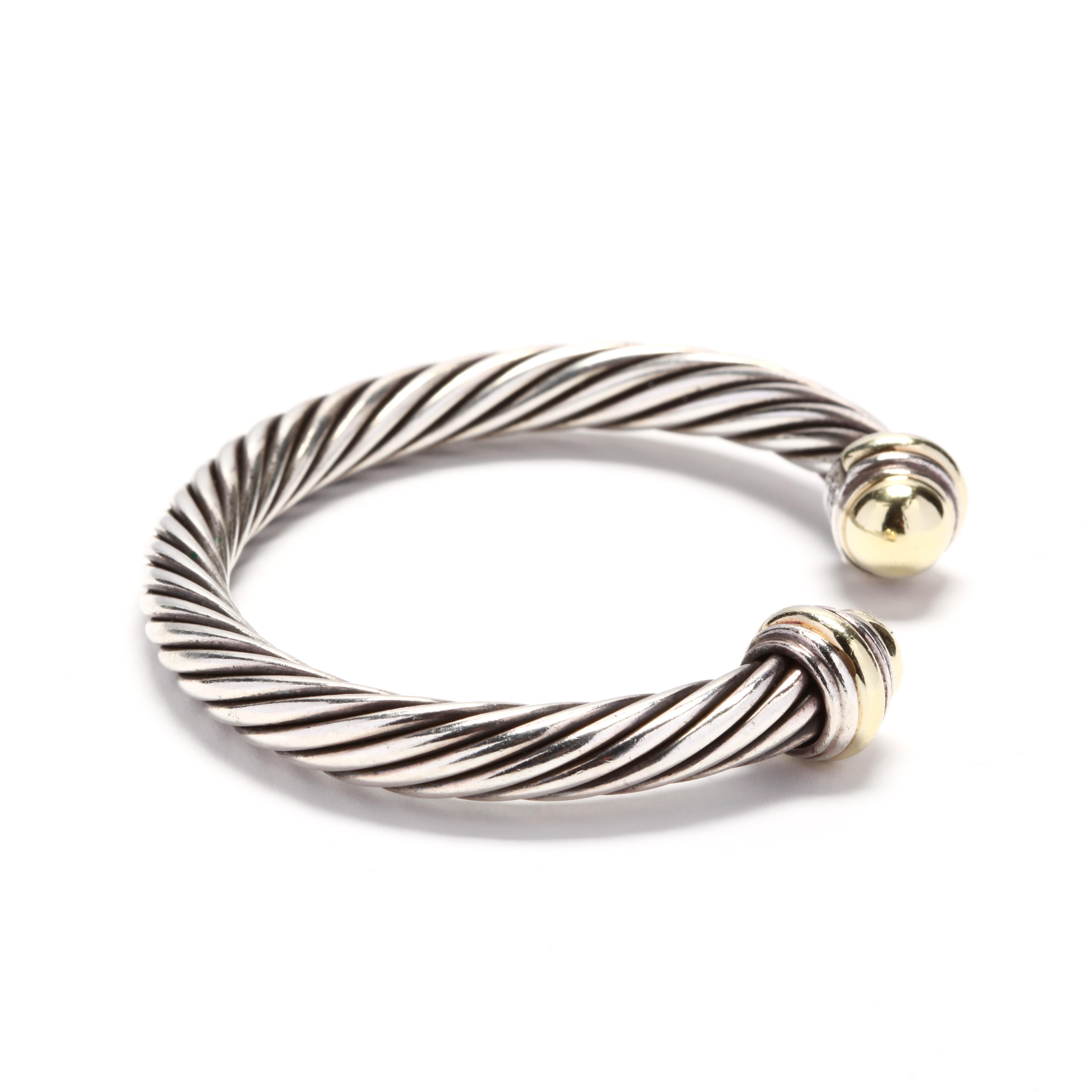 A David Yurman 14 karat yellow gold and sterling silver gold dome cuff bracelet. This 7mm cuff bracelet features a cable motif cuff with gold dome endcaps. The endcaps has a minor dent but not noticeable when worn.



Length: 6.25 in. with a 5/8 in.