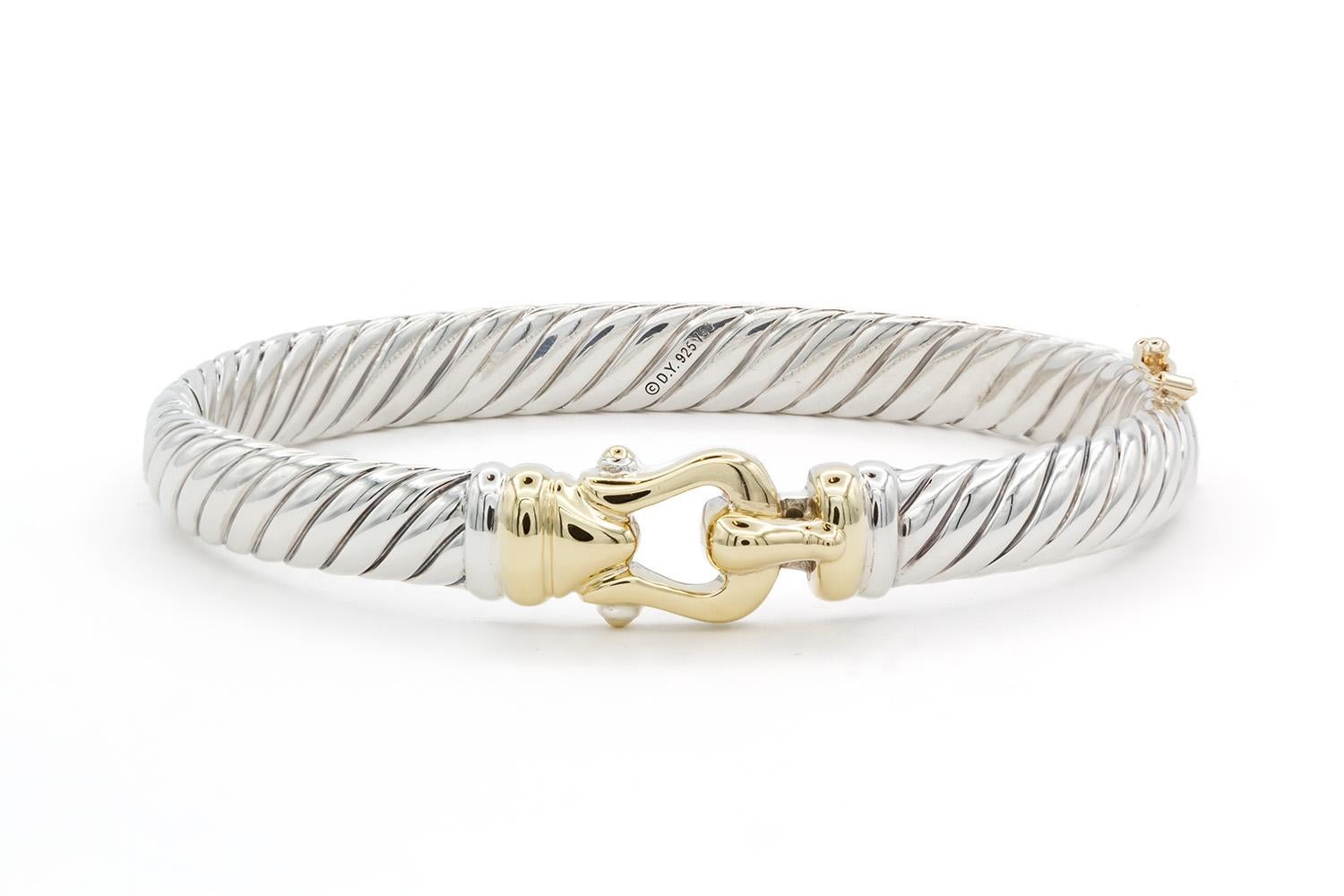 We arepleased to offer this David Yurman Two Tone Hinged Buckle Bracelet Bangle. This bracelet features David Yurmans classic cable design and is fashioned from sterling silver & 18k yellow gold. The bracelet measures 7mm wide and will fit up to a