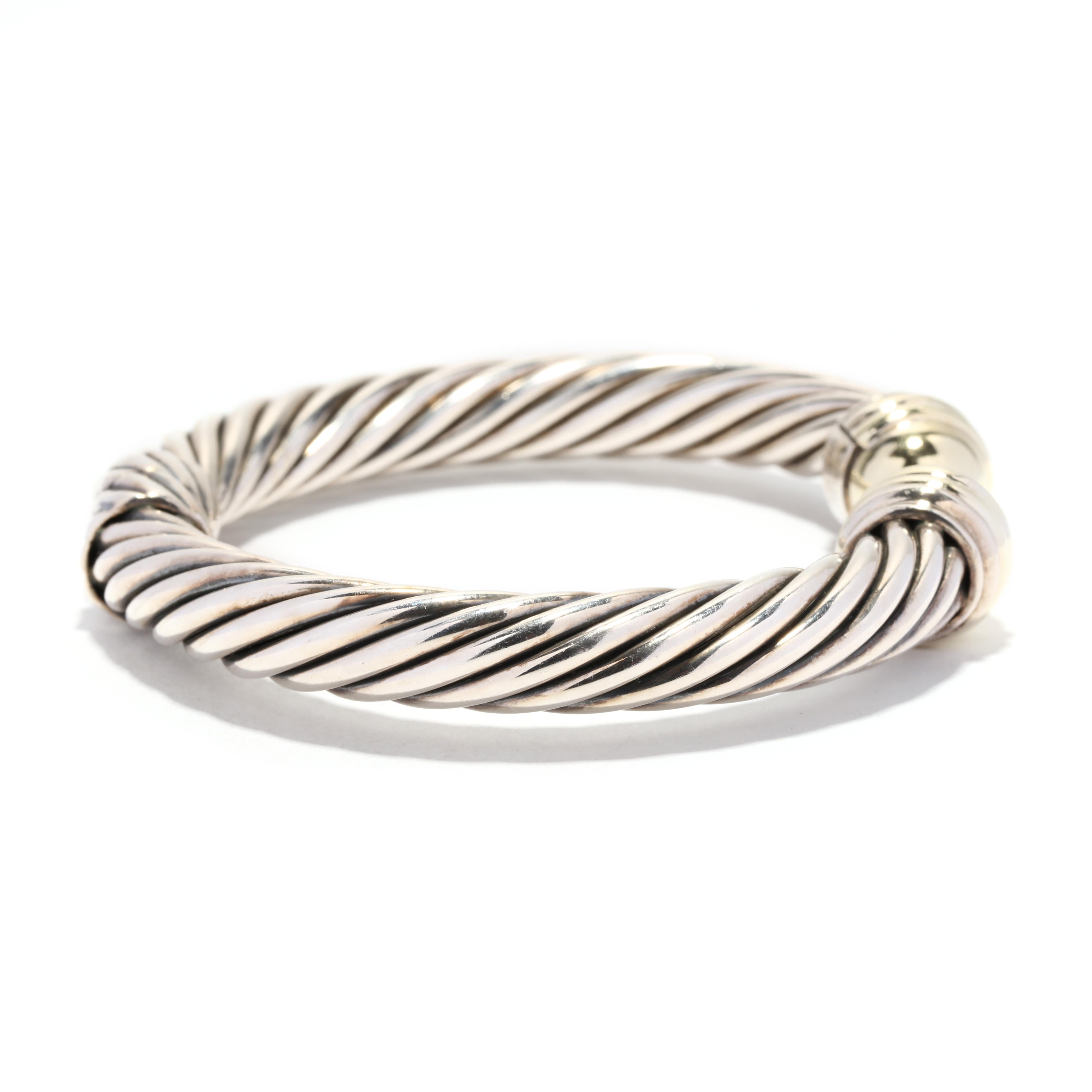 A vintage David Yurman 14 karat yellow gold and sterling silver large gold dome hinged cable cuff bracelet. This simple cuff bracelet features a hinged closure with silver cable motif cuffs and with yellow gold dome end caps. This is the David