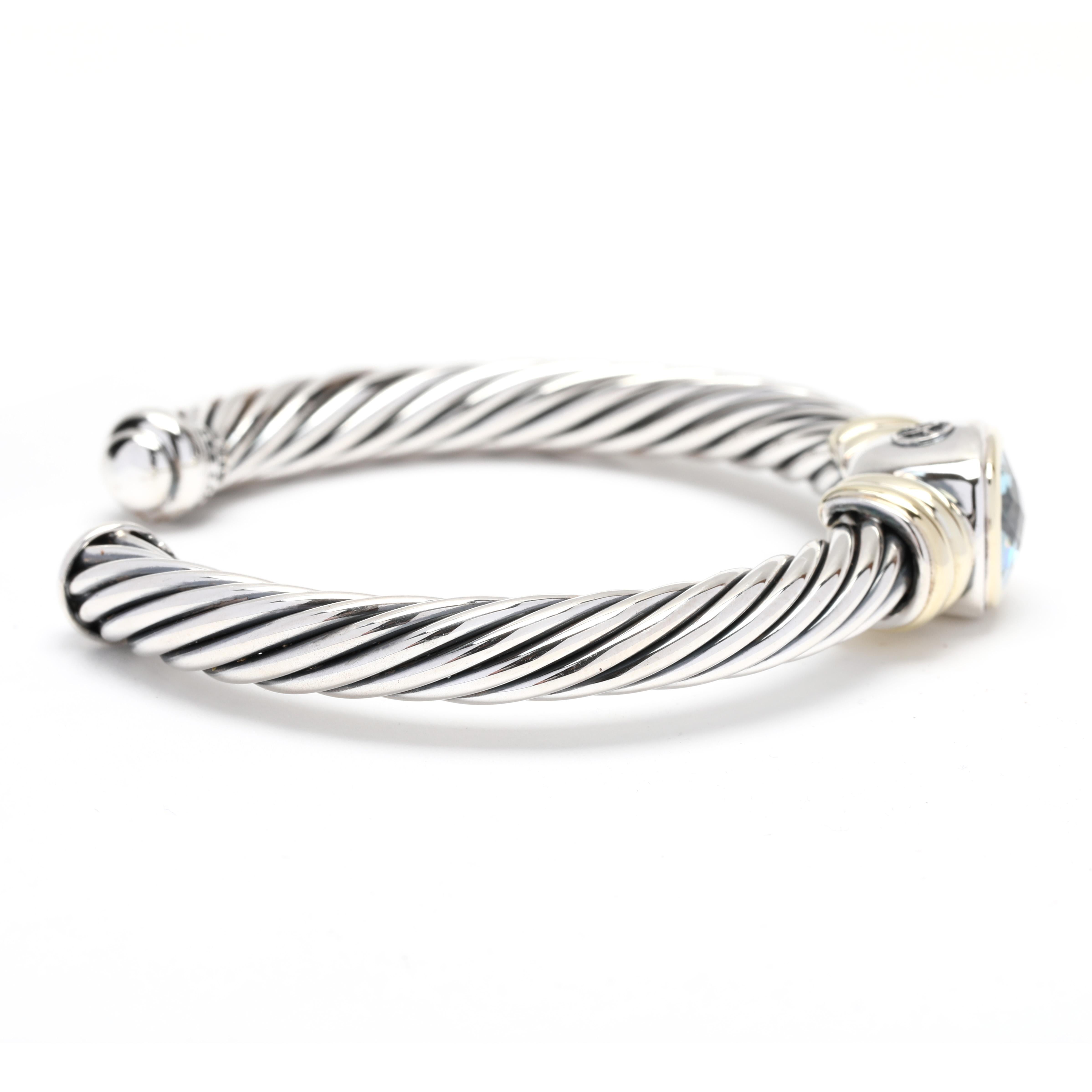 This beautiful David Yurman Noblesse Blue Topaz Cuff Bracelet is crafted from 14K yellow gold and sterling silver and features a captivating horizontal cable cuff. A coveted piece from the Noblesse Collection, the stylish design is completed with a
