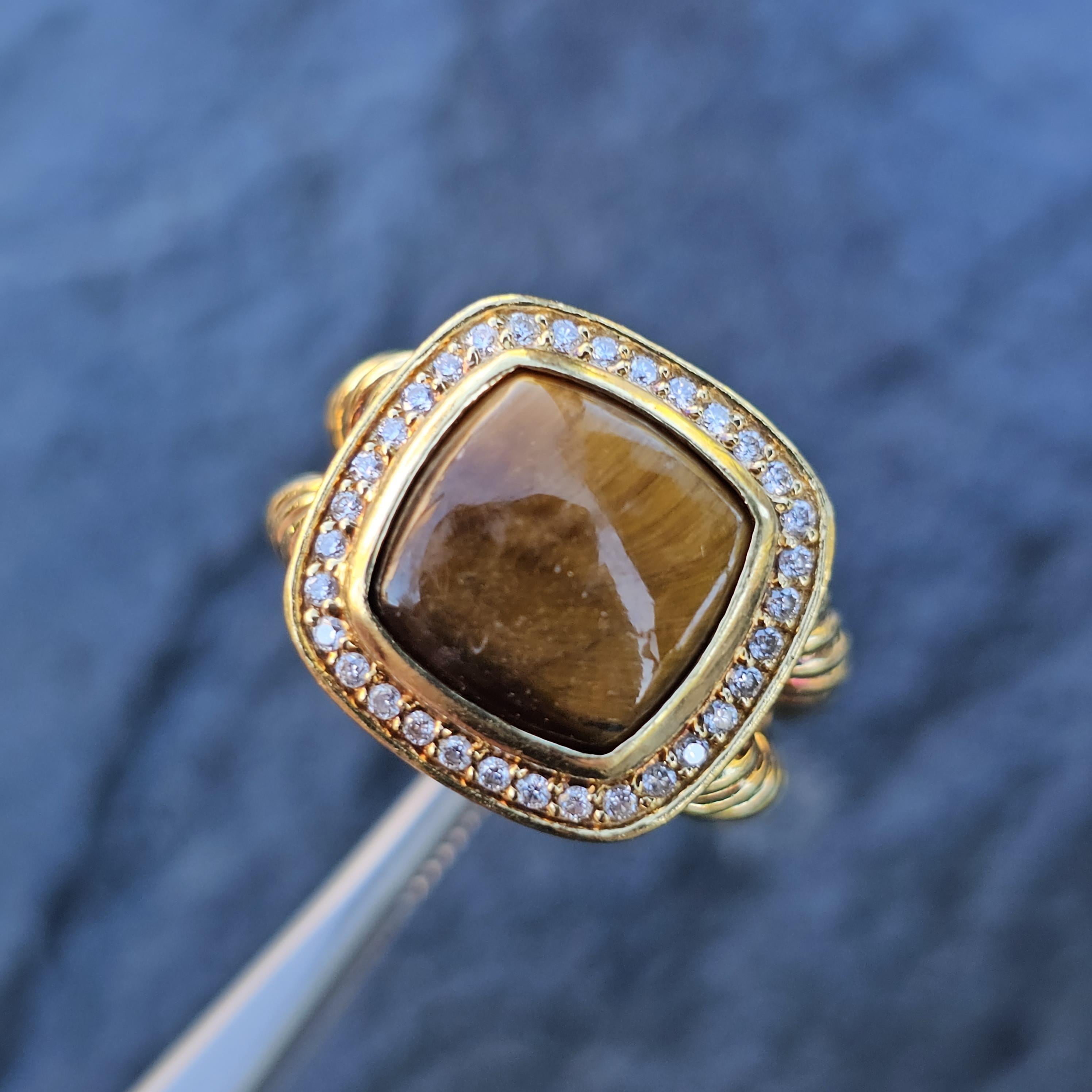 Aquí tenemos un anillo David Yurman Albion del siglo XXI con un cautivador Ojo de Tigre como piedra principal, rodeado por un halo de diamantes blancos. El anillo está fabricado en lujoso oro amarillo de 18 quilates, mostrando una armoniosa mezcla