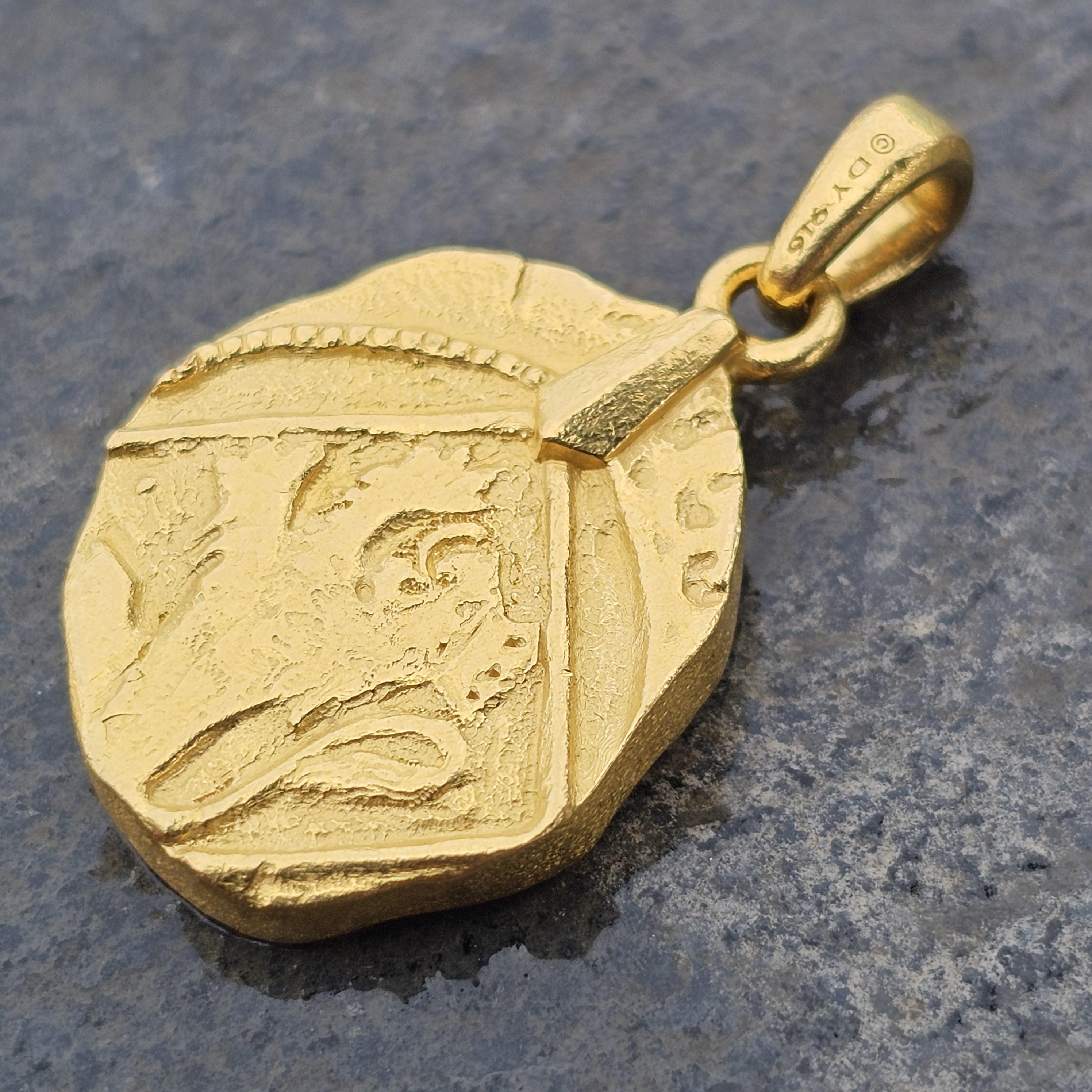 This is a David Yurman Shipwreck Coin Amulet Pendant Necklace. The pendant is crafted from 22k yellow gold, showcasing a textured, irregular shape with intricate detailing. The design features a raised, abstract motif, adding a unique character to