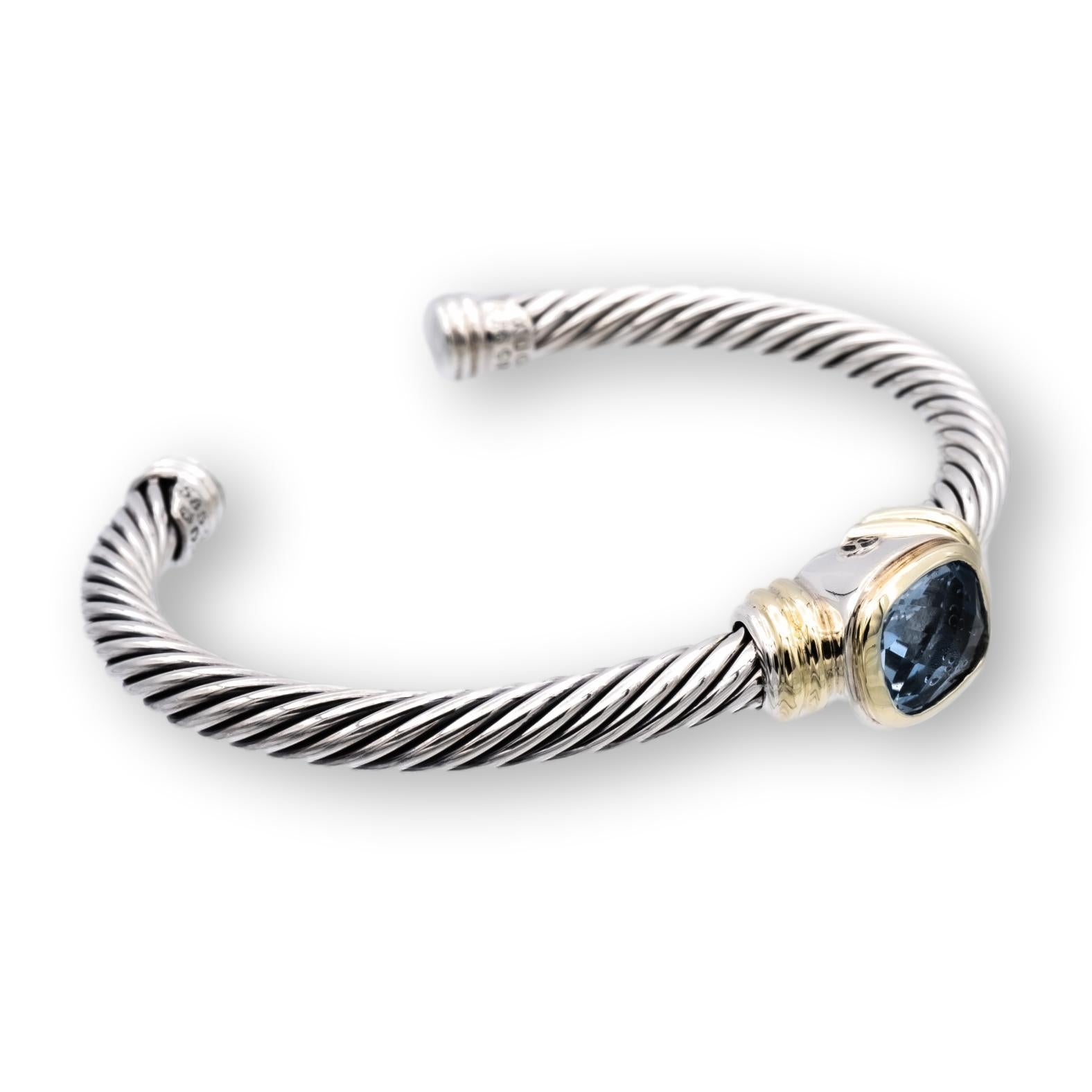 David Yurman open cuff bracelet from the Noblesse collection finely crafted in sterling silver featuring a medium deep blue topaz cushion cut center set in 14 karat yellow gold bezel. Bracelet measures 5mm wide and fits wrists up to 6.25