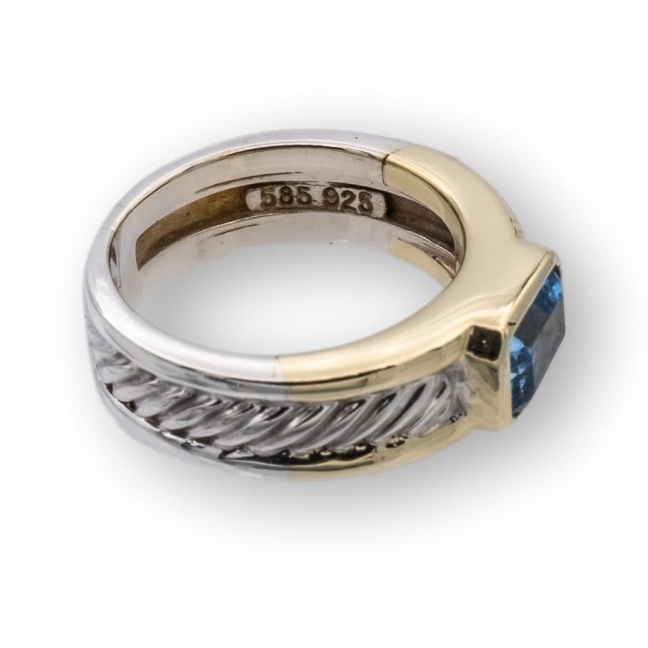 David Yurman ring from the Cable Classics collection finely crafted in sterling silver featuring a rectangular cut crisp blue topaz in the center set in a 14K yellow gold bezel. The center stone weighs 0.60 carats approximately. Width of band is