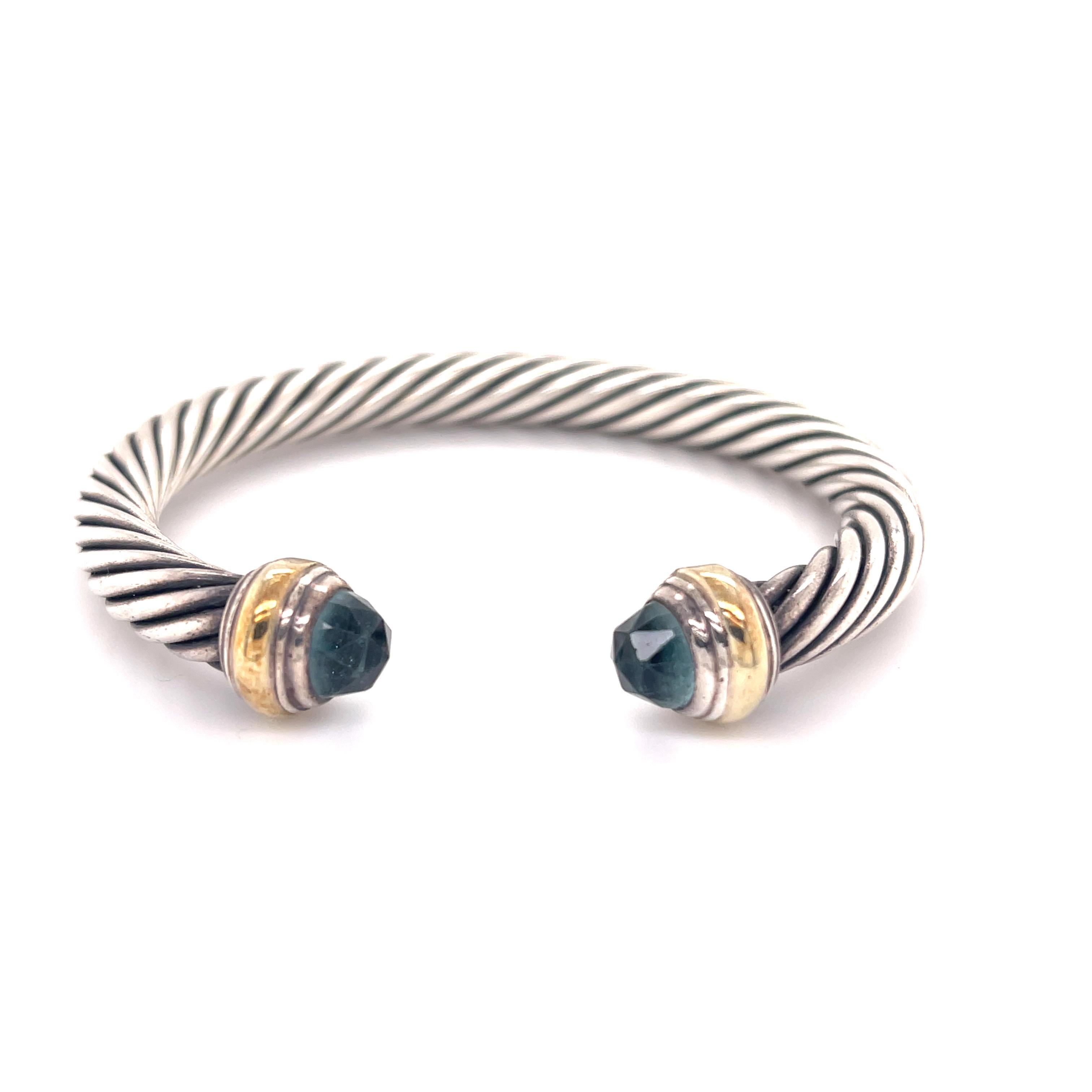 One lady's designer made brush finished, textured, silver and 14K yellow gold, blue topaz bangle, cuff bracelet. The bracelet measures approximately 6.00 inches in length tapering to 5.00mm in width and weighs a total of 41.90 grams. Engraved with