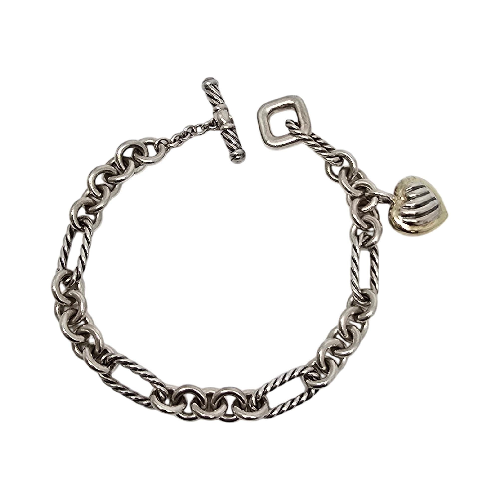 Sterling silver with 18K yellow gold accent cable heart charm toggle bracelet by David Yurman.

This classic Yurman bracelet features alternating smooth round links with twist rope oval links with a toggle closure. The heart dangle is Yurman's