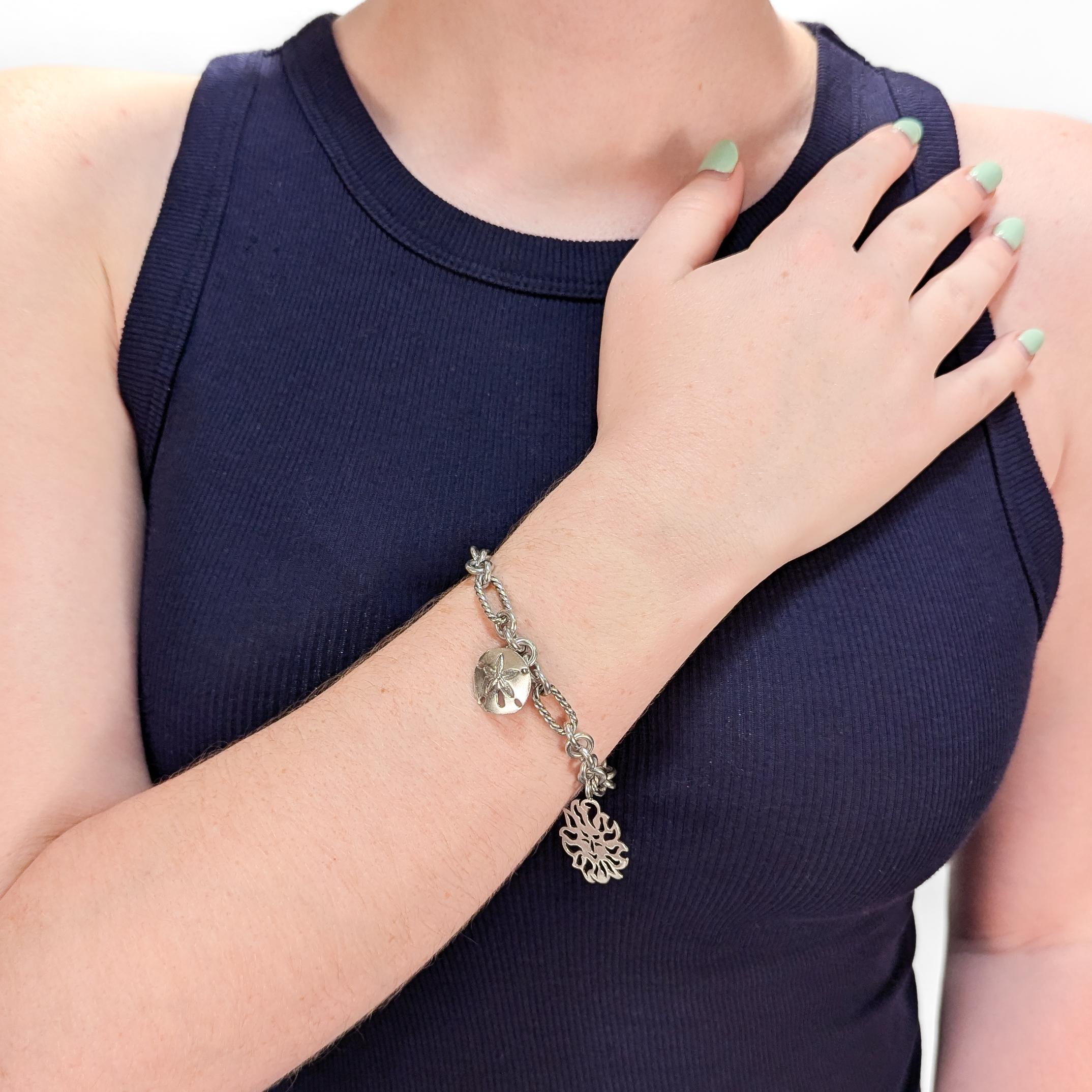 A fine signed silver charm bracelet. 

By David Yurman.

In sterling silver with 18 karat gold elements.

Comprised of a Figaro style chain with a ribbon bow charm, a smiling sun charm, and a sand dollar charm. The ribbon bow with gold