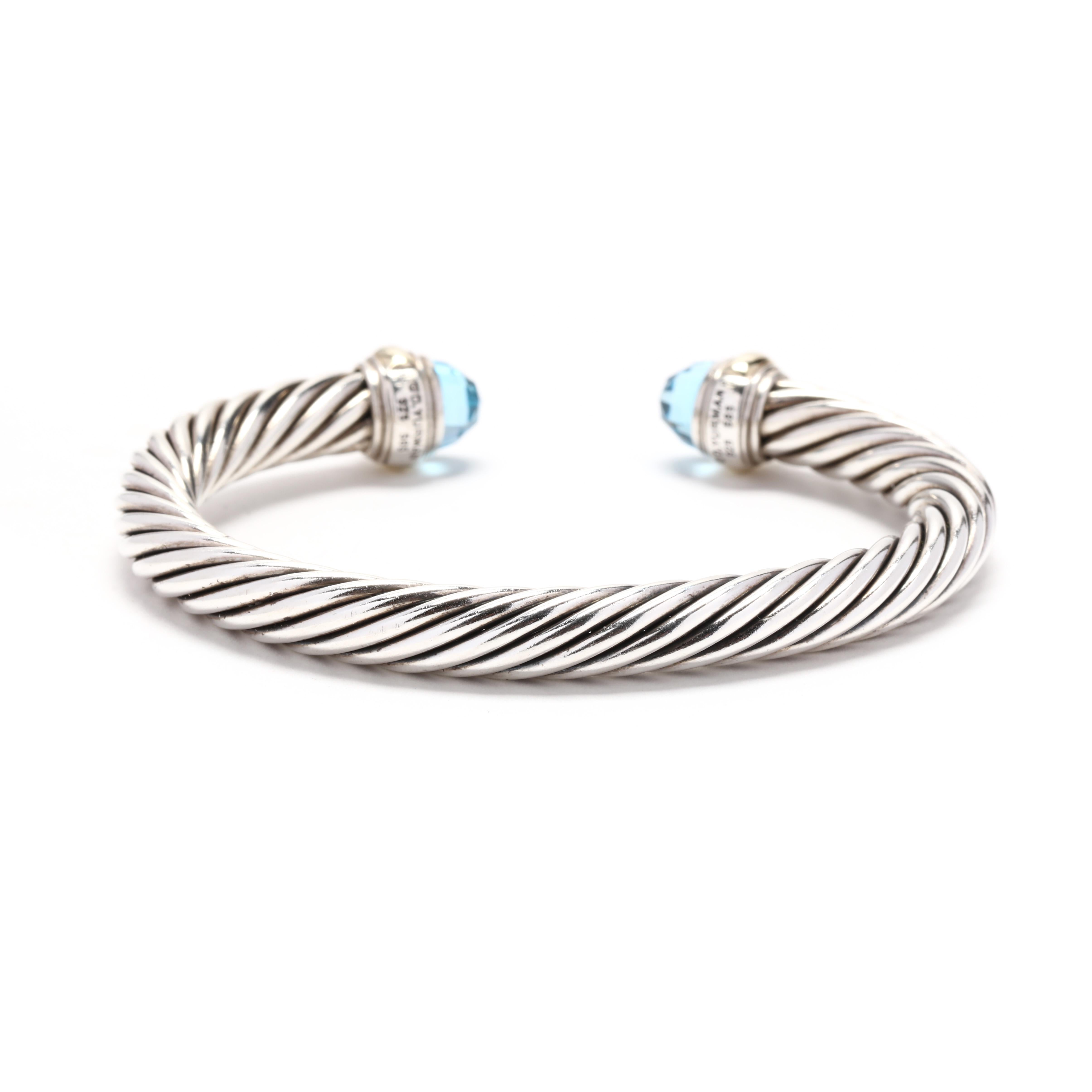 A 14 karat yellow gold and sterling silver blue topaz cuff bracelet by David Yurman. This bracelet features a silver cable cuff design with faceted blue topaz end caps and yellow gold detailing.



Length: 6.25 in.; adjustable



Width: 7