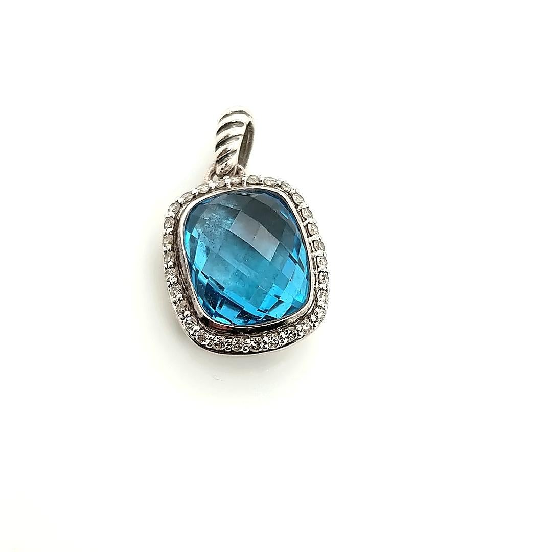 This is a beautiful all original pendant by David Yurman in sterling silver with a lovely blue topaz center framed by a row of glittering white diamonds! The blue topaz center is fantastically cut, creating a dancing flashing of light over the