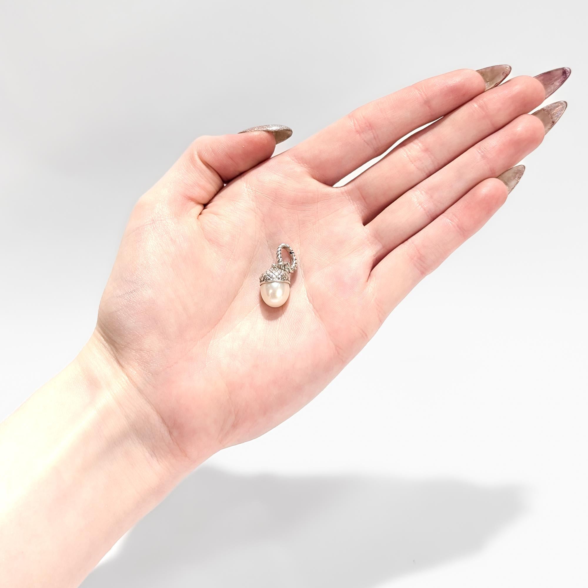 A fine signed silver & pearl pendant enhancer.

By David Yurman.

In sterling silver. 

In the form of an acorn with a pearl as the acorn's body bezel-set in a silver cupule.

With an integral bail, jump ring, and a pendant clip to the top of the