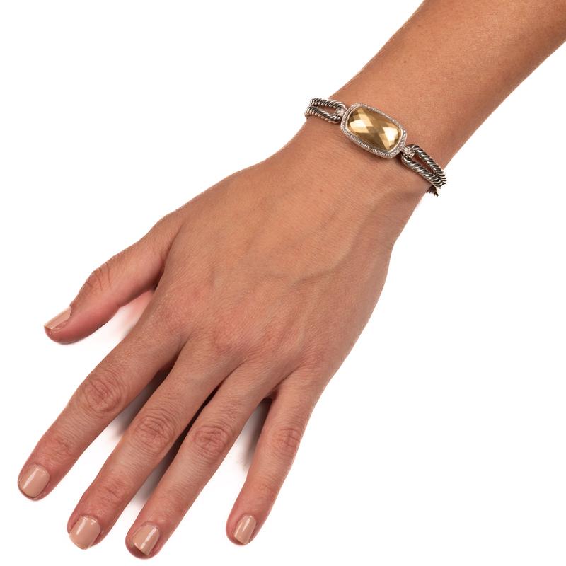 This bracelet from David Yurman features a double cable hinged bangle crafted in sterling silver with a hammered 18 karat yellow gold dome accented by pave-set round diamonds with an approximate weight of 0.45 carats. This is a size small.