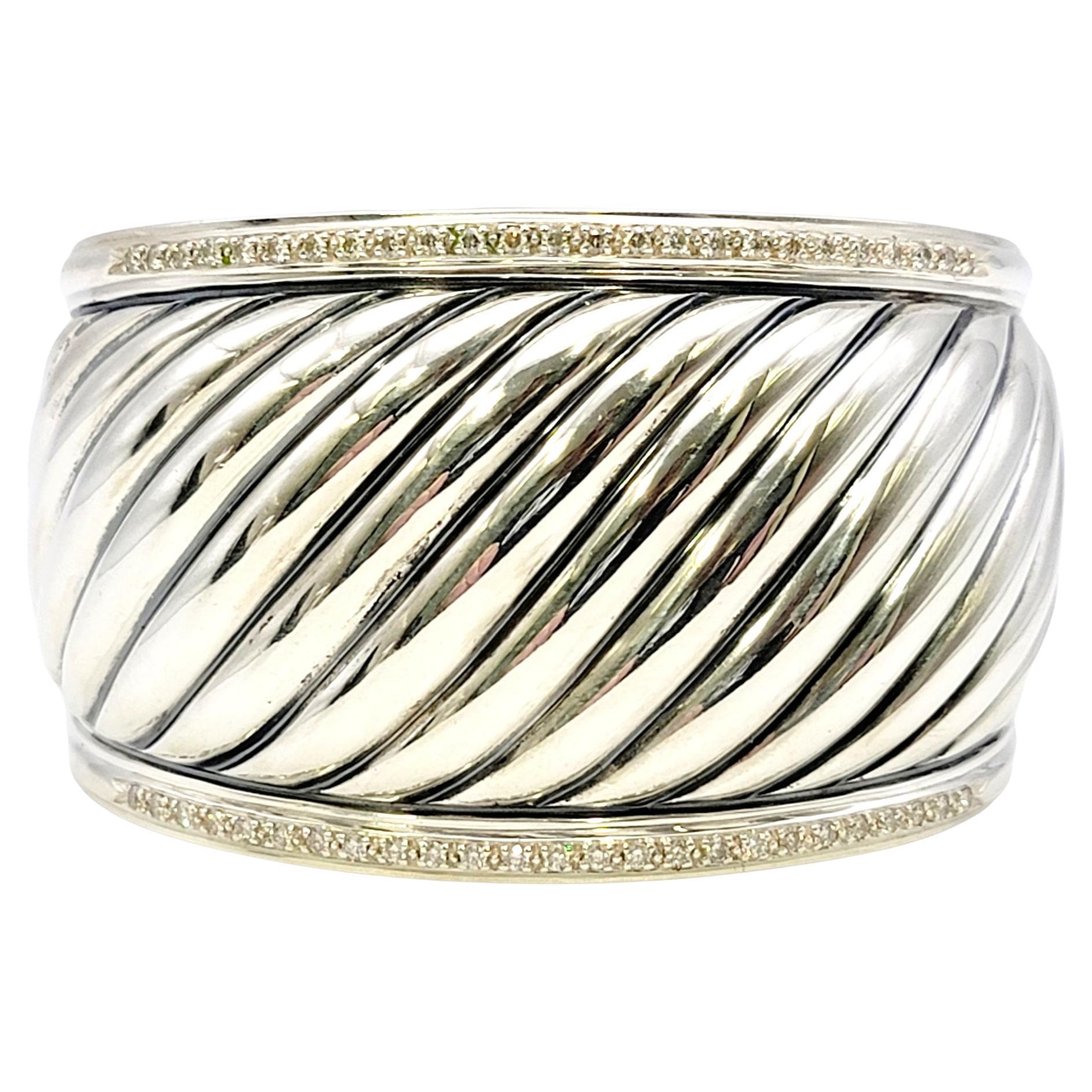 Bold and beautiful designer cable cuff bracelet by jewelry designer, David Yurman. Sleek and sculptured, this bracelet features a wide ridged cable design accented by sparkling natural diamonds along the edges. The polished sterling silver really