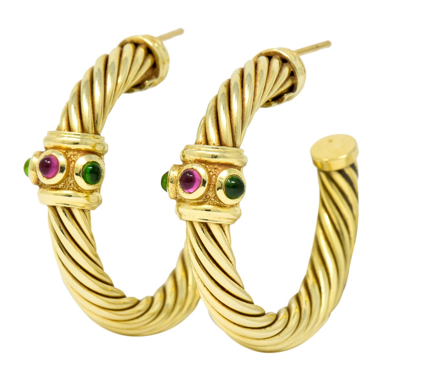 Hoop style earrings designed as twisted cable motif with polished gold terminals

Each featuring a textured gold station bezel set with round cabochon cut green tourmalines and a rhodolite garnet measuring approximately 2.5 mm

Post and friction