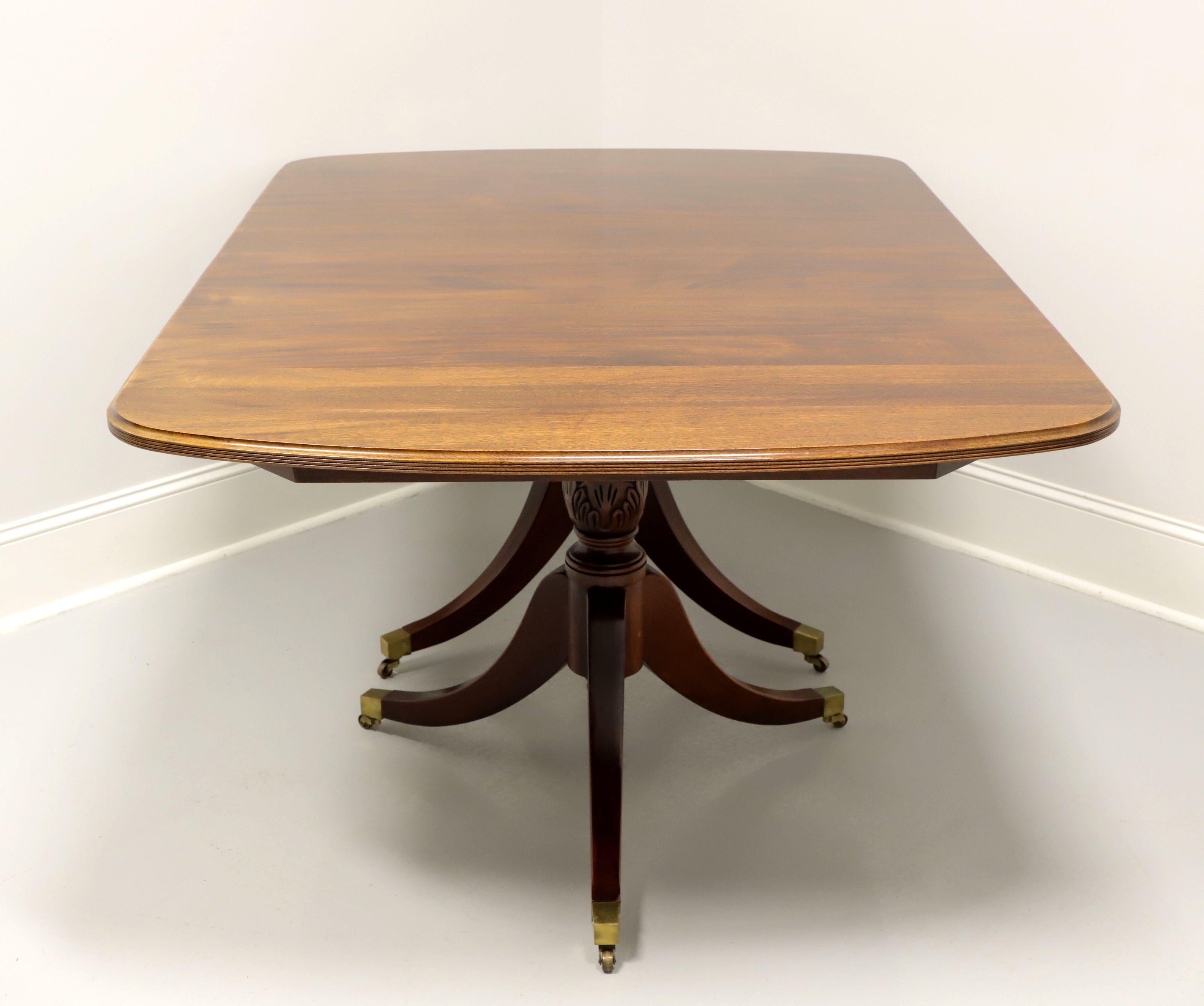A Traditional style rectangular dining table by Davis Cabinet Company. Mahogany with brass casters, rounded corners to top, ribbed edge, double pedestal base, three curved legs with brass toe caps and casters. Includes three extension leaves for