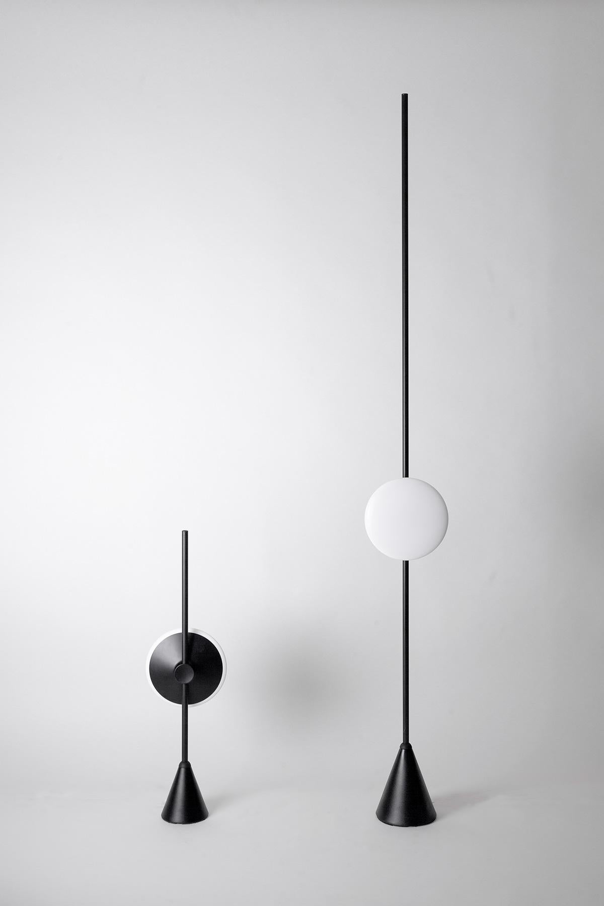 Dawn to dusk table lamp - Haberdashery 

Measures: W 210 x H 740 x D 125mm

Material: 

Puck head: 
Aluminium
White polycarbonate
Material Base:
Aluminium with cast iron
Finishes:
Black anodised aluminium

The Dawn to Dusk range evokes
