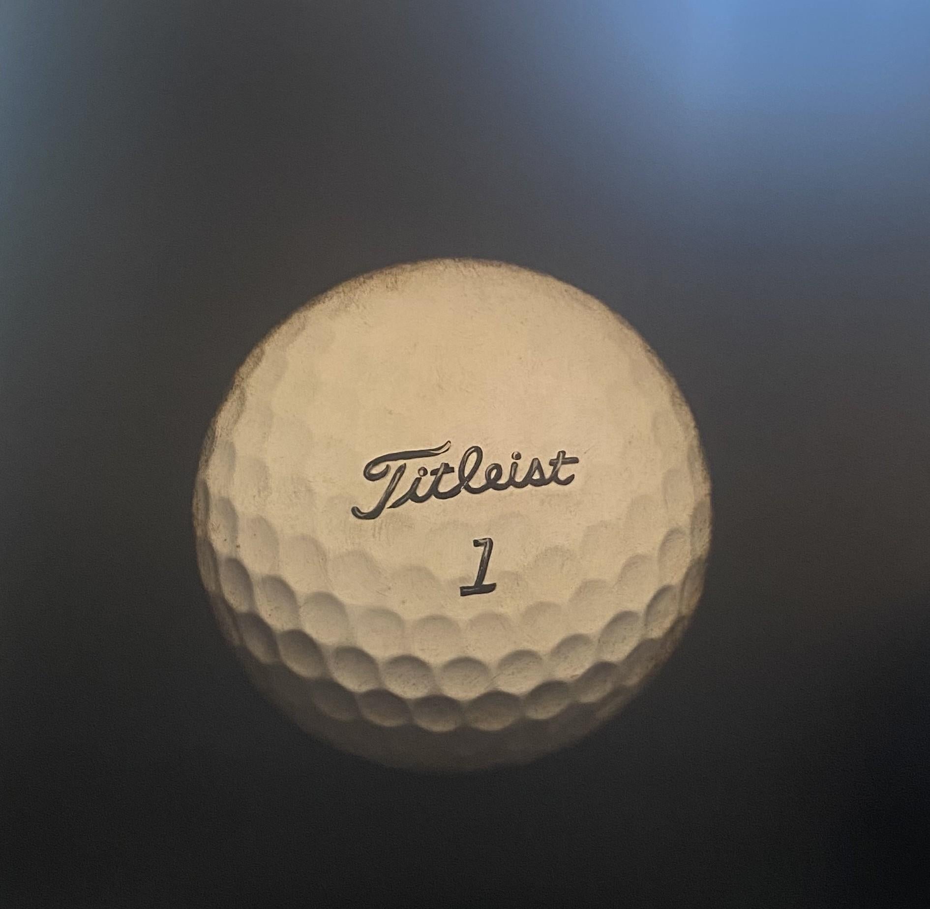 "Fore-thought" de Dawne Raulet es una sorprendente pintura fotorrealista de una sola bola de golf Titleist suspendida sobre un fondo dramático y sombrío. Con sus detalles de precisión y su iluminación suave y atmosférica, esta obra de técnica mixta