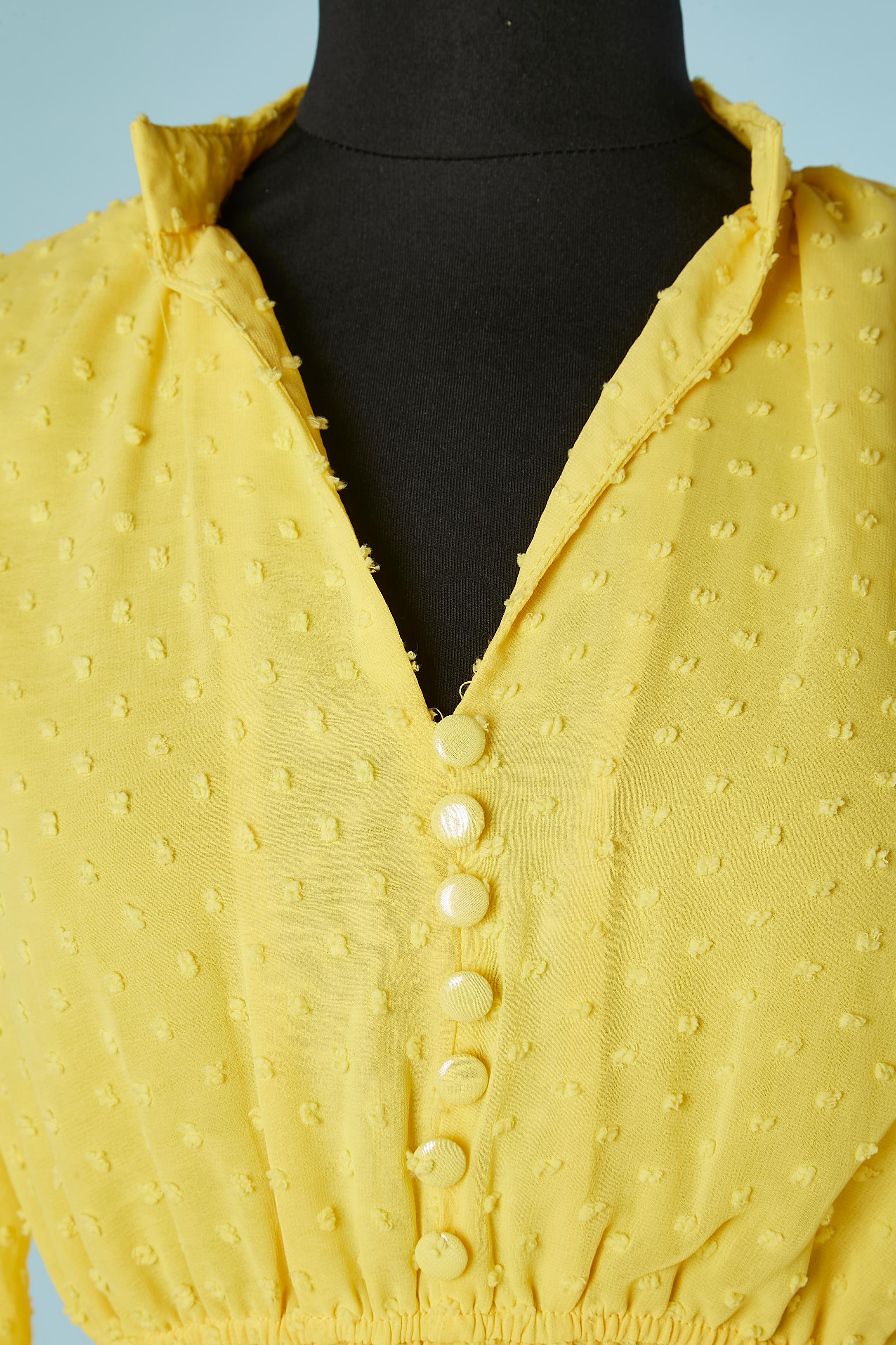 Day dress in yellow plumetis with belt and ruffles. No fabric composition tag but probably polyester. Decoratives buttons in fabric covered with transparent plastic on the top middle front. Belt in the same fabric. Elastic band on the waist. 
SIZE